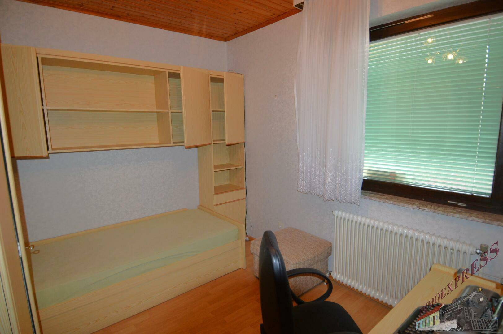 Schlafzimmer mit Einzelbett, Einbauschränken und Fenster mit Jalousien.