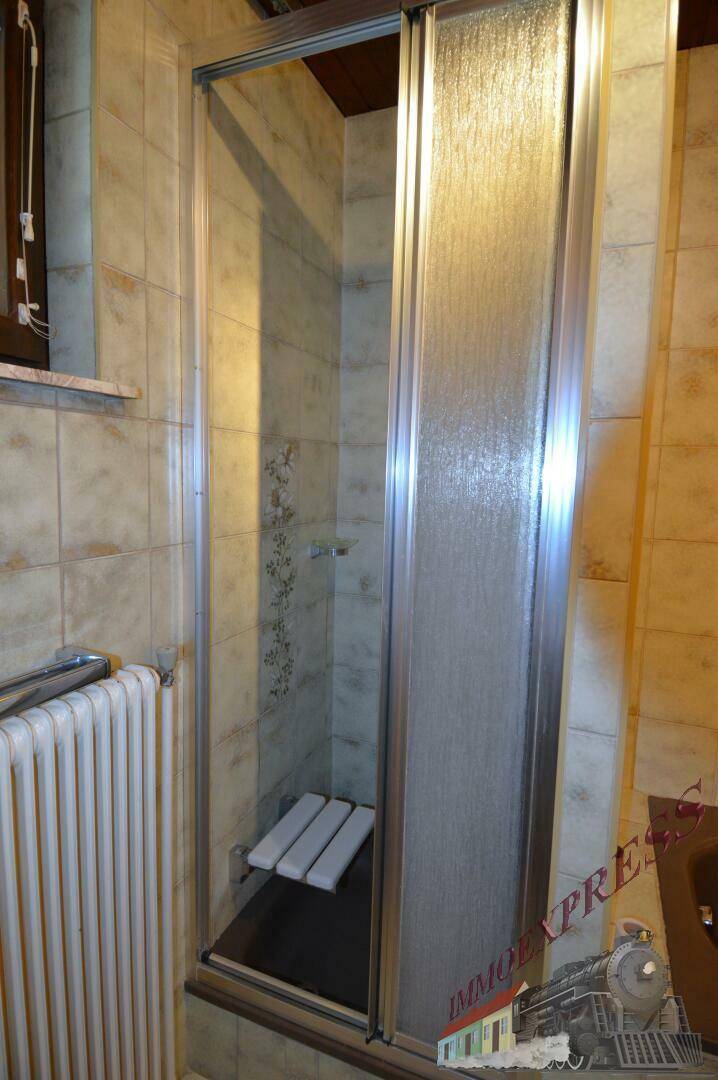 Duschbereich mit Glasabtrennung und Sitzgelegenheit in einem gefliesten Badezimmer.