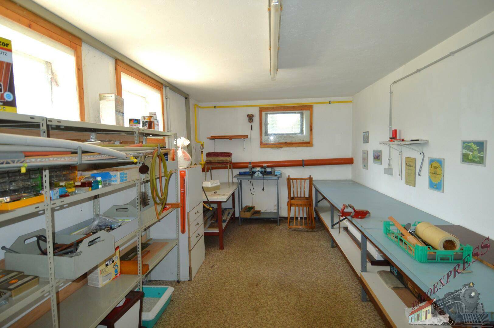 Großer Werkstattraum im Keller mit Arbeitsflächen, Regalen und Fenstern.