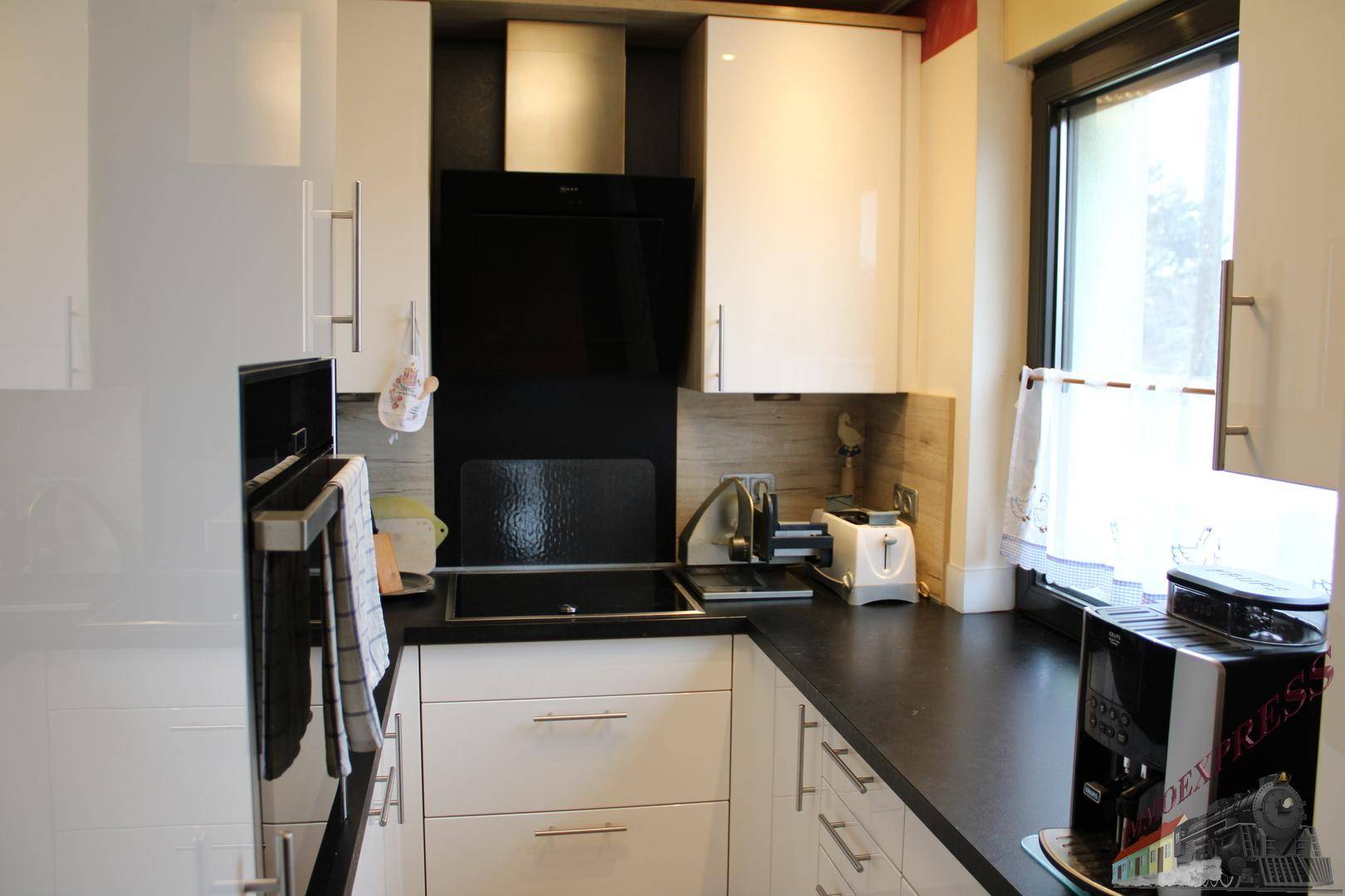 Moderne Küche mit weißen Hochglanzschränken, dunkler Arbeitsplatte und Fenster.
