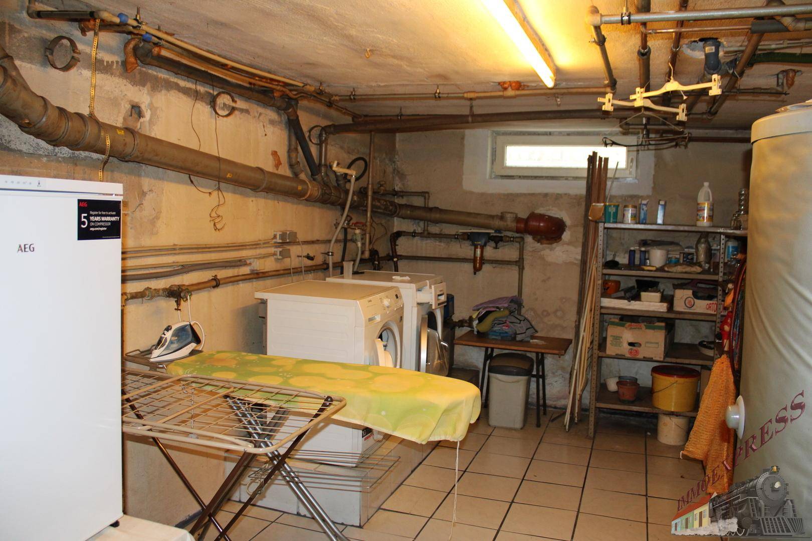 Waschküche im Keller mit Waschmaschine, Trockner und Bügelbrett.