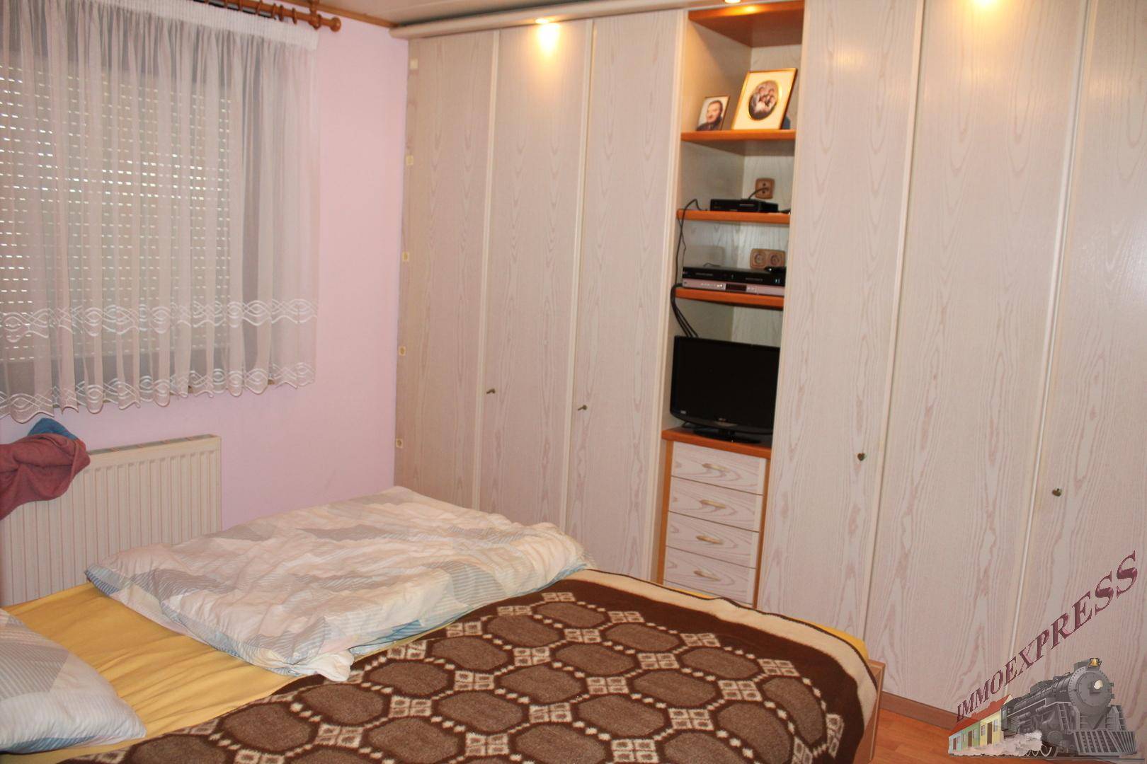 Schlafzimmer mit großem Bett, Einbauschränken und einem Fenster mit Vorhängen.