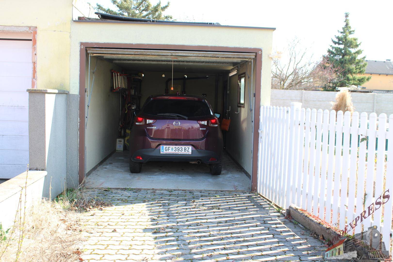 Einzelgarage mit einem geparkten Auto und gepflasterter Zufahrt.