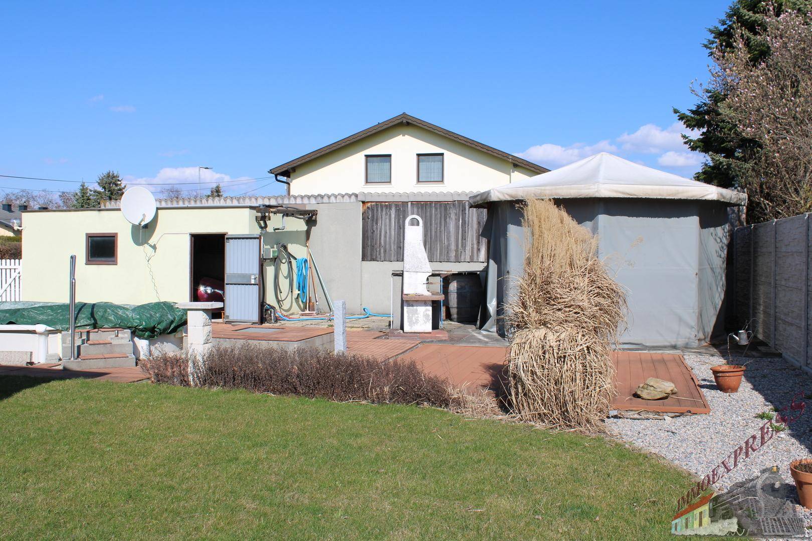 Hinterhof mit Rasenfläche, Gartenlaube, Grillplatz und einem weiteren Gebäude im Hintergrund.