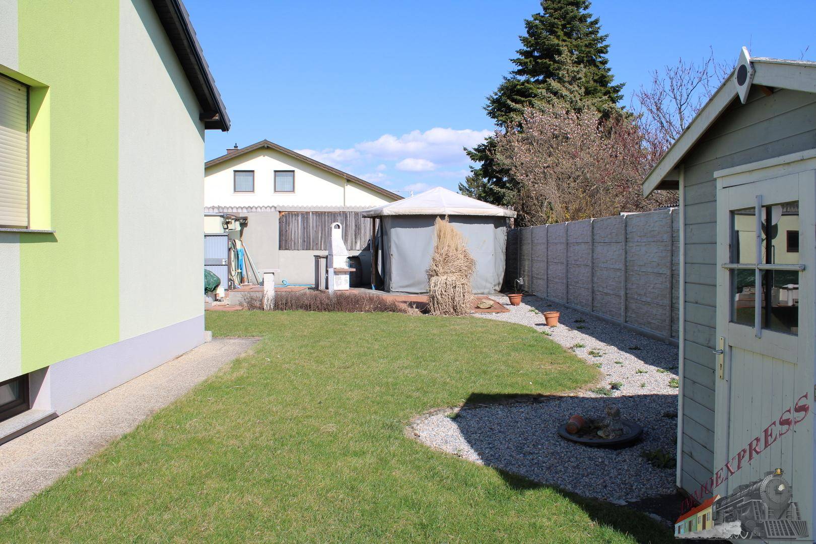 Gartenbereich mit Rasenfläche, Kieswegen und einem kleinen Gartenhaus.