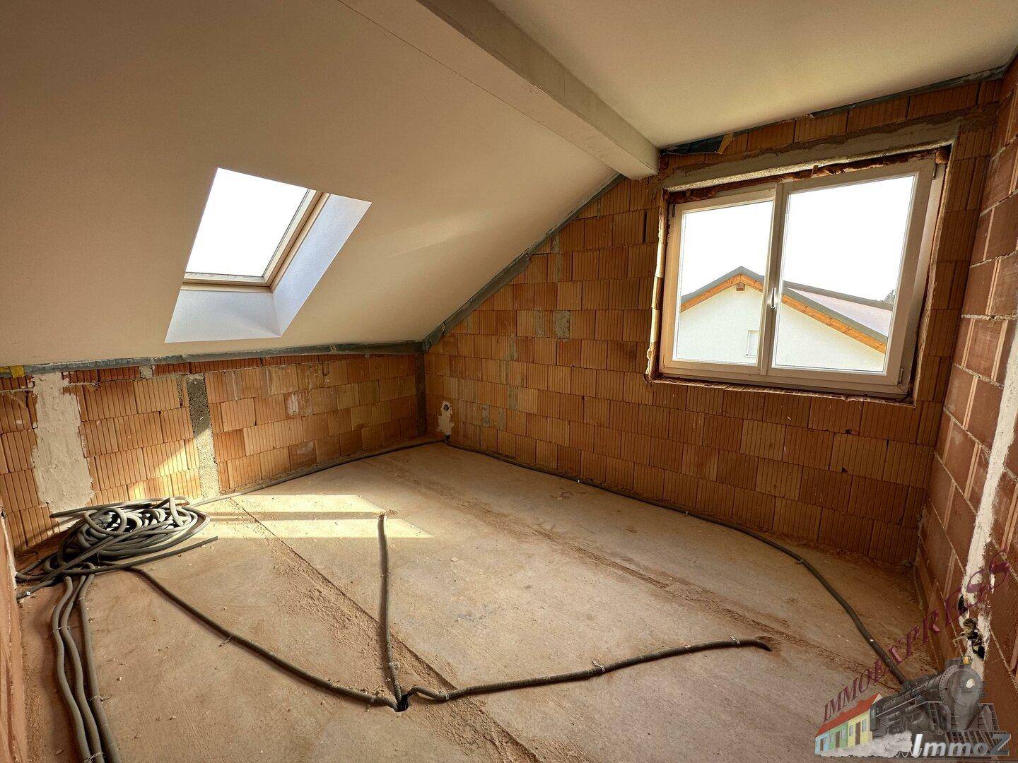 Rohbauzimmer im Dachgeschoss mit Fenster, Dachschräge und einem weiteren Dachfenster.