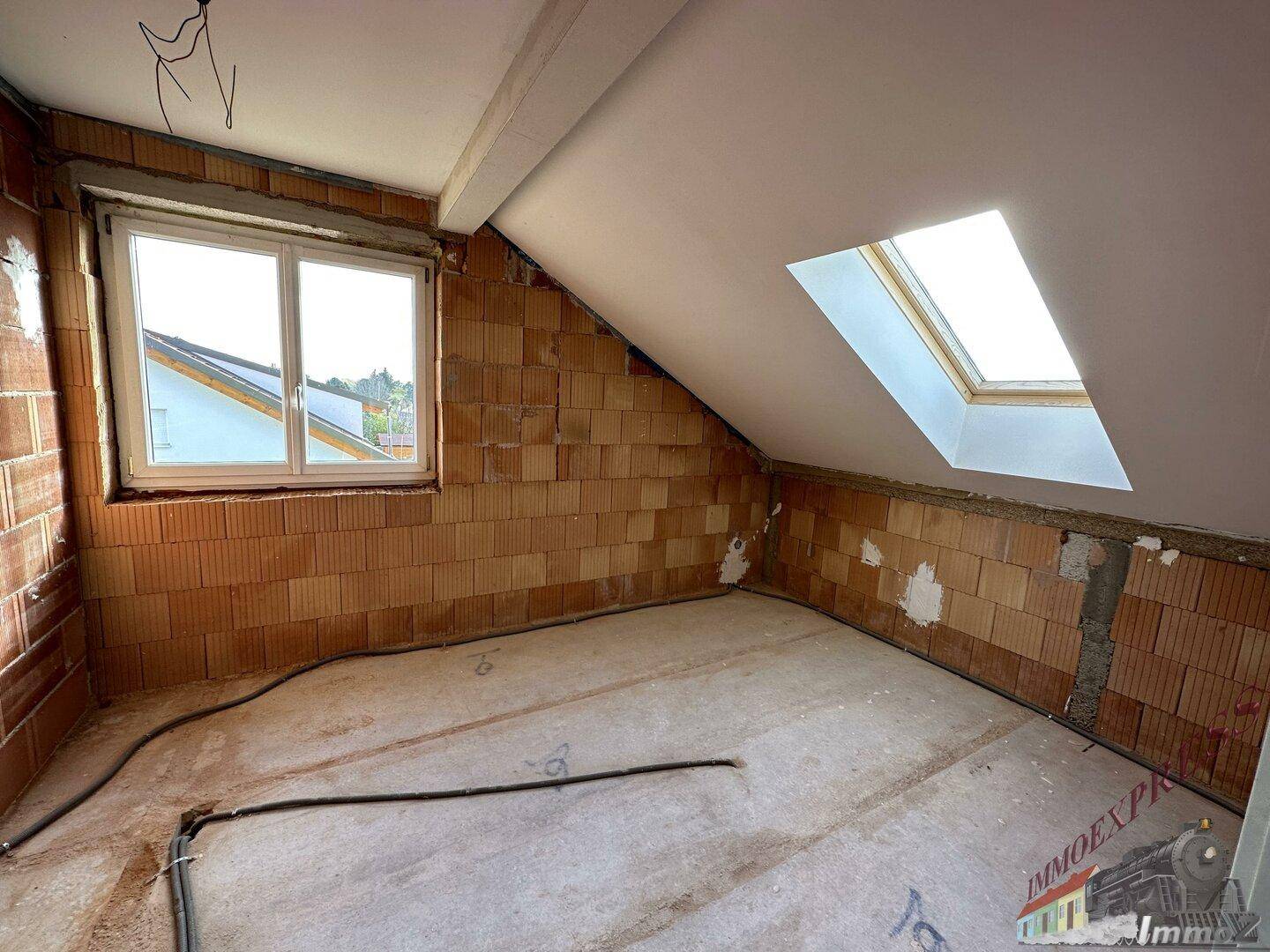 Dachgeschosszimmer im Rohbau mit Fenster, Dachschräge und zusätzlichem Dachfenster.