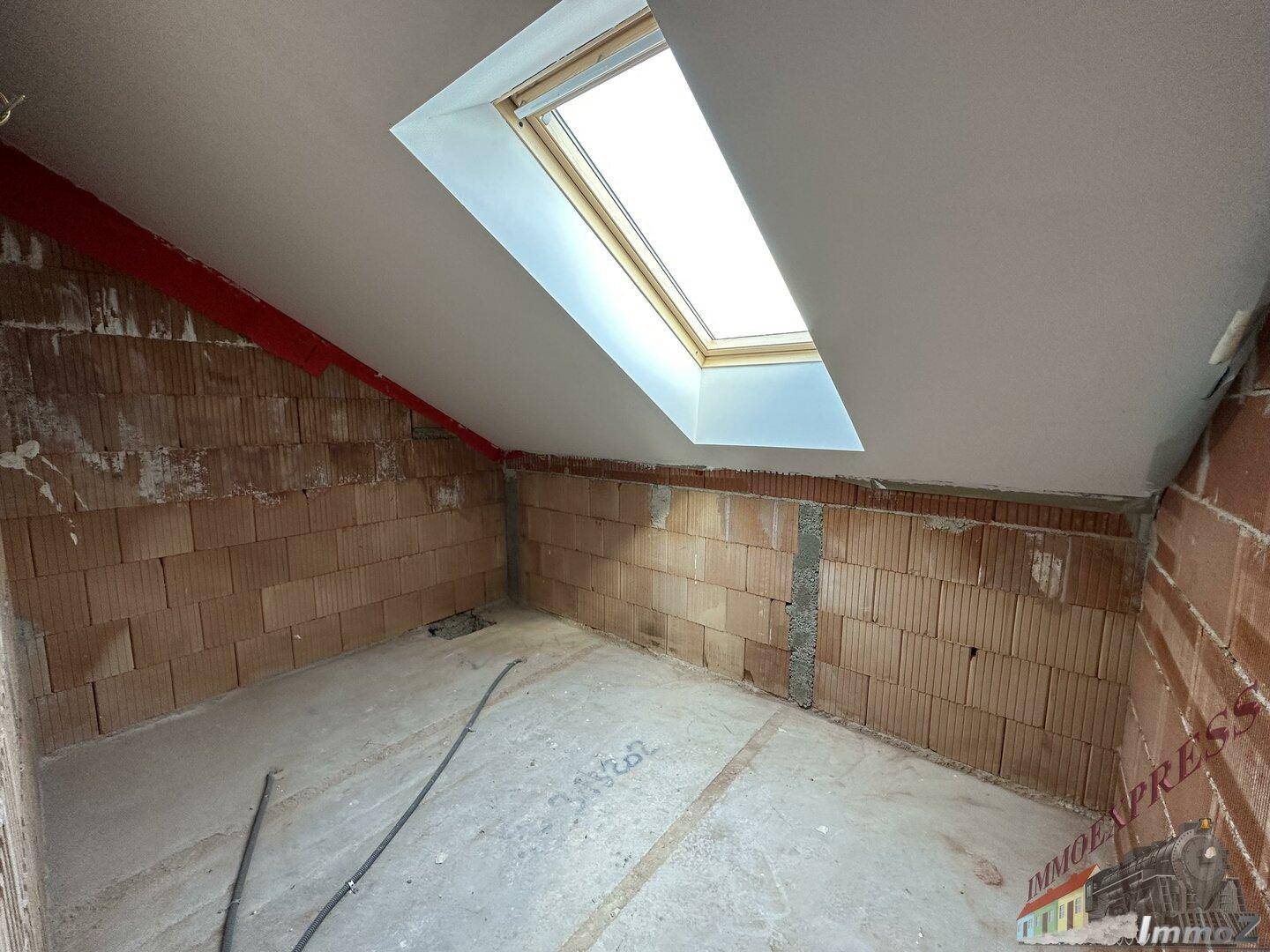 Unfertiges Dachgeschosszimmer mit Ziegelwänden, Dachschräge und einem Dachfenster.