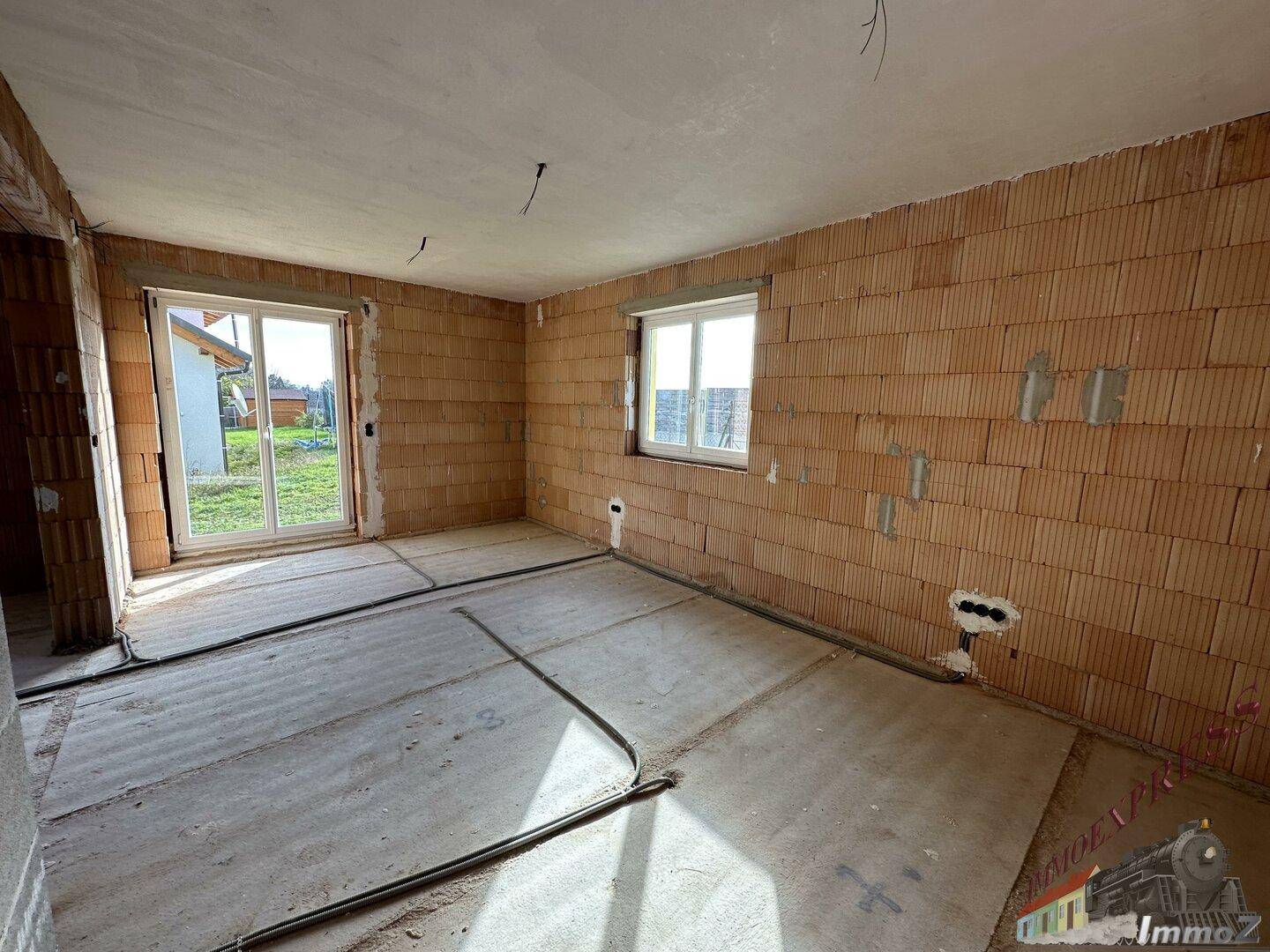 Rohbauzimmer mit Ziegelwänden, Estrichboden und Zugang zum Außenbereich.