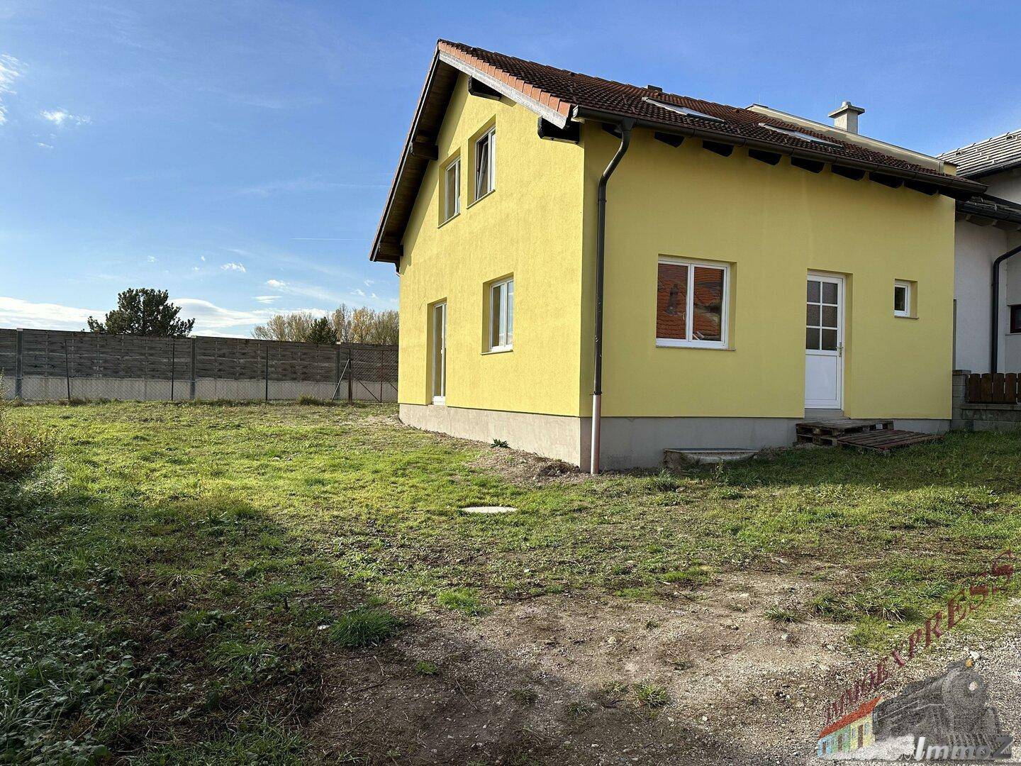 Rückansicht des gelben Hauses mit großem, ungenutztem Grundstück und Zaun.