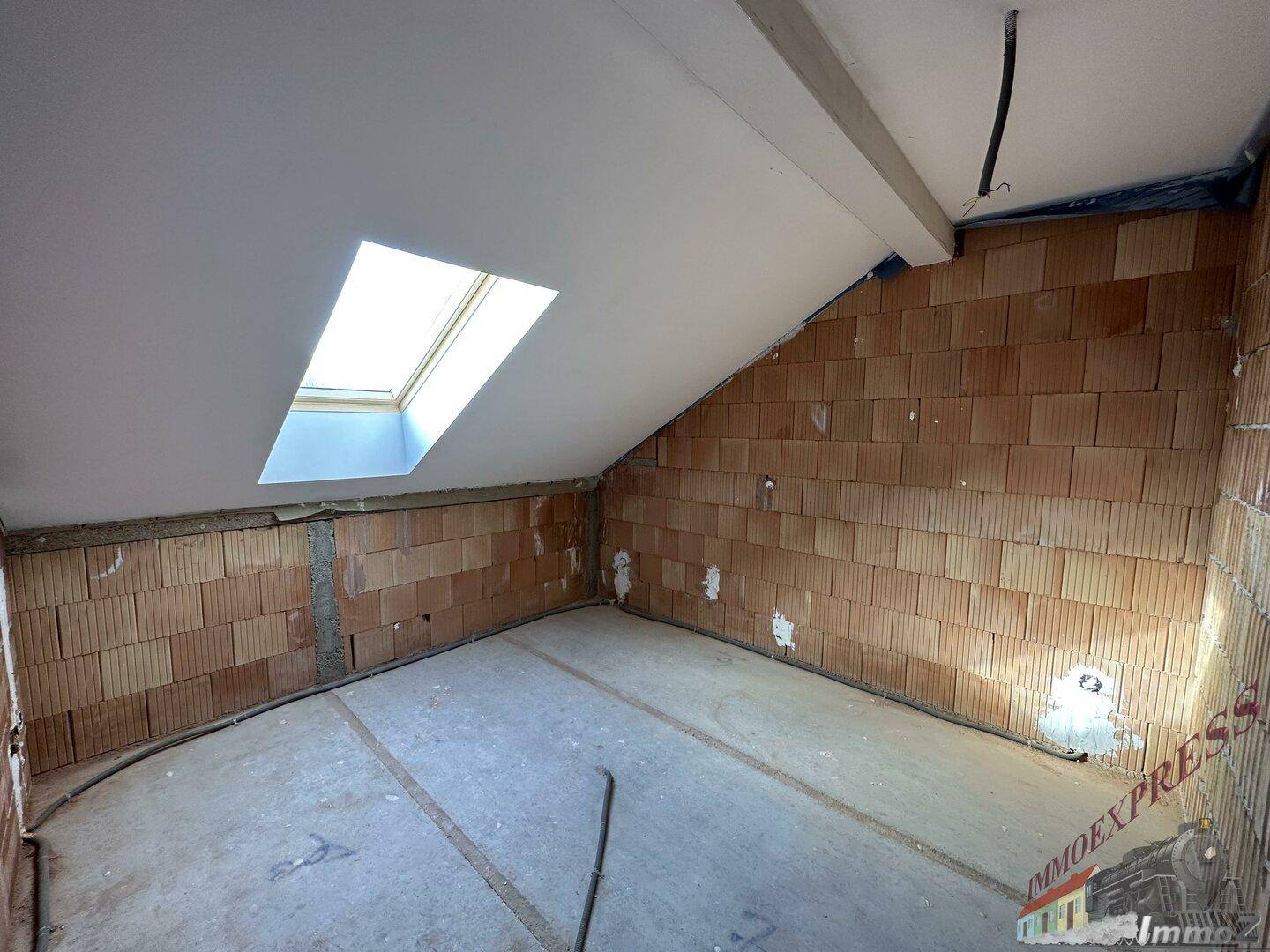 Dachgeschossraum im Rohbau mit Ziegelwänden, Dachschräge und einem hellen Dachfenster.