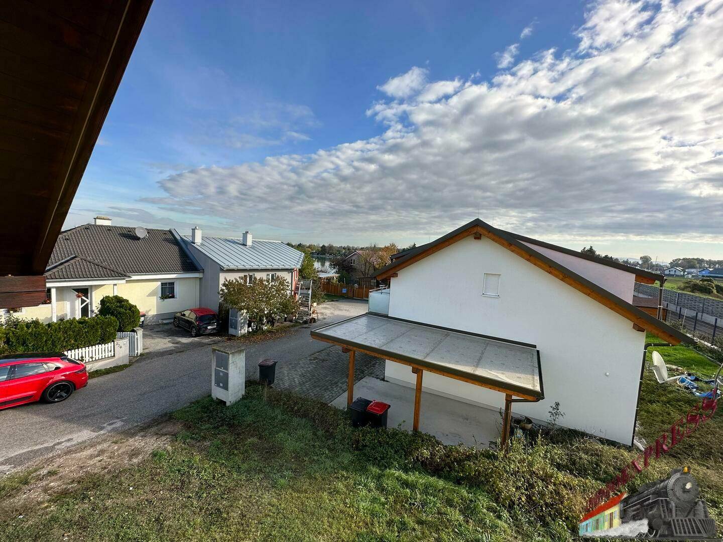 Blick über die Nachbarschaft mit Wohnhäusern und einem Carport unter blauem Himmel.
