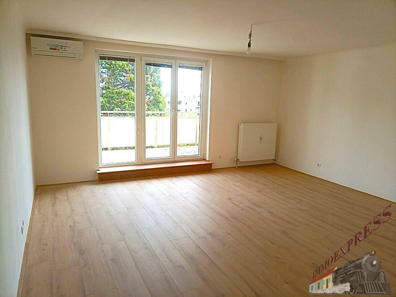 Heller Wohnraum mit Holzboden, großen Fenstern und Klimaanlage, bereit zur Einrichtung.