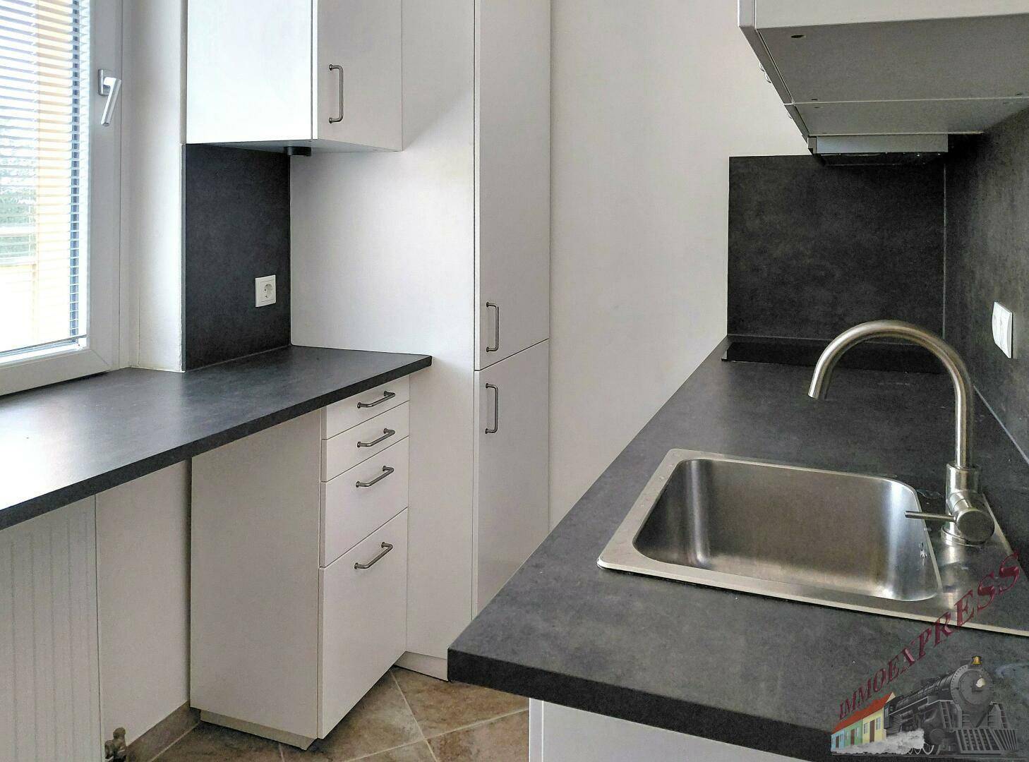 Funktionale Küchenzeile mit weißen Schränken, dunkler Arbeitsplatte und Spülbecken unter dem Fenster.