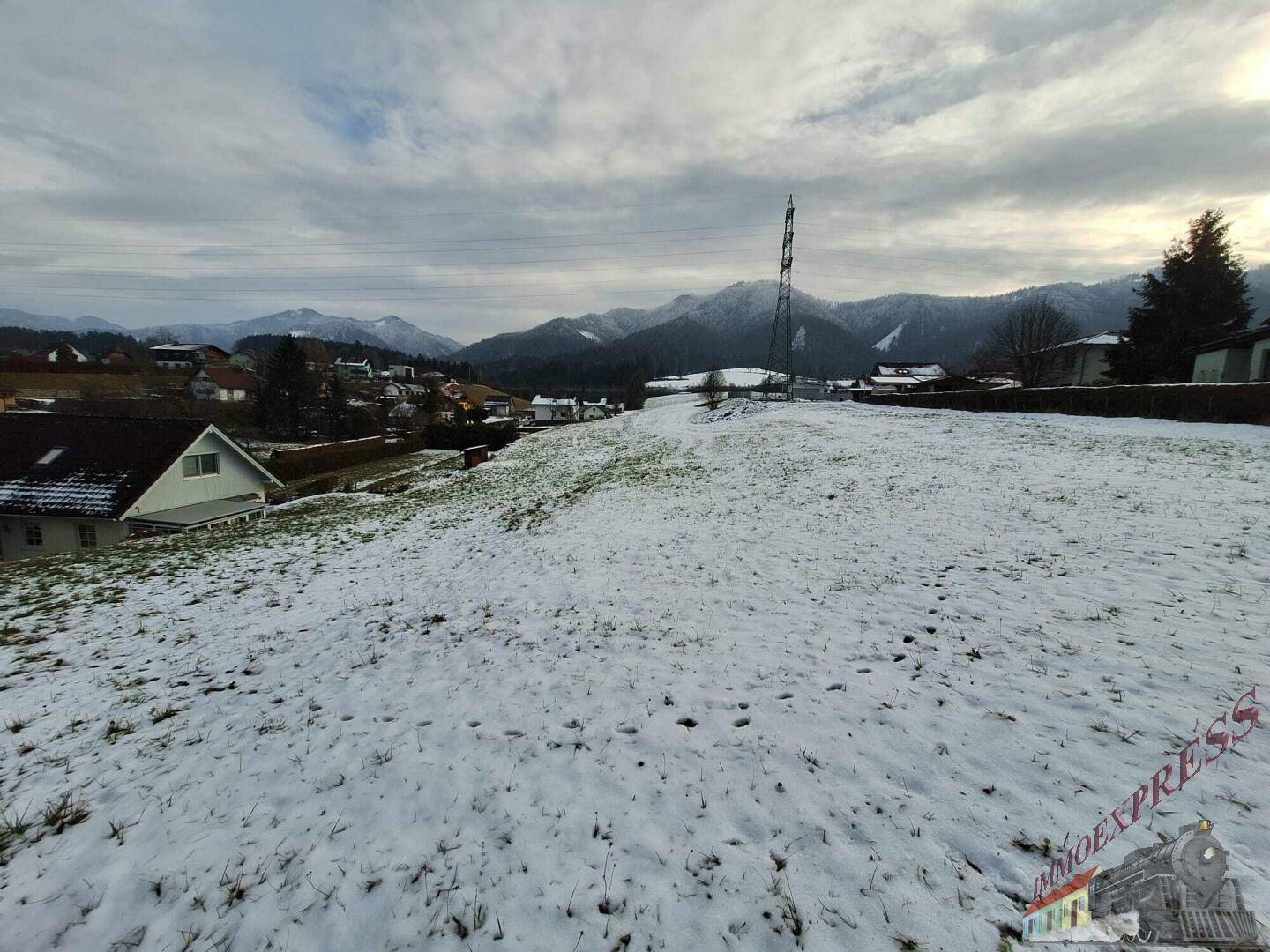 Schneebedecktes Grundstück mit Blick auf die umliegende Berglandschaft und Häuser im Tal.