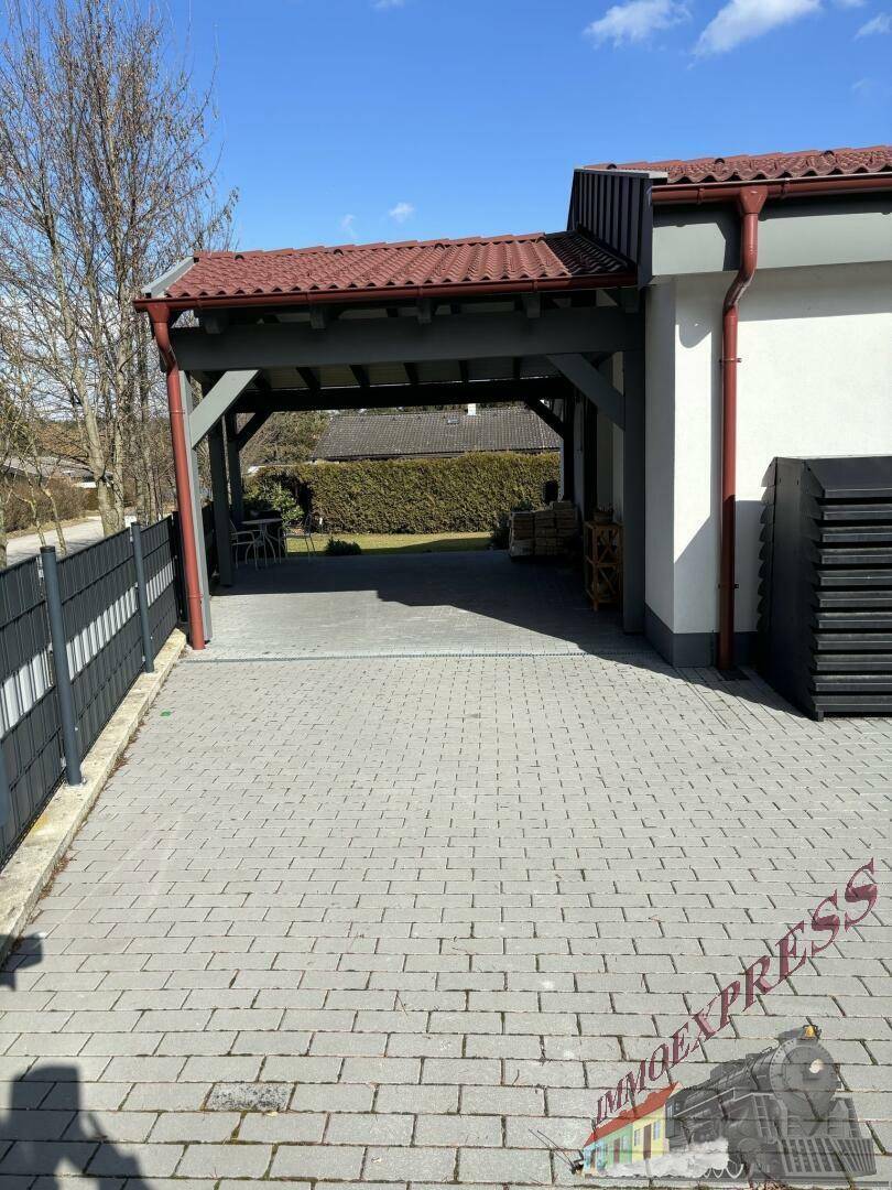 Gepflasterte Einfahrt führt zu einem überdachten Carport-Bereich neben dem Haus.