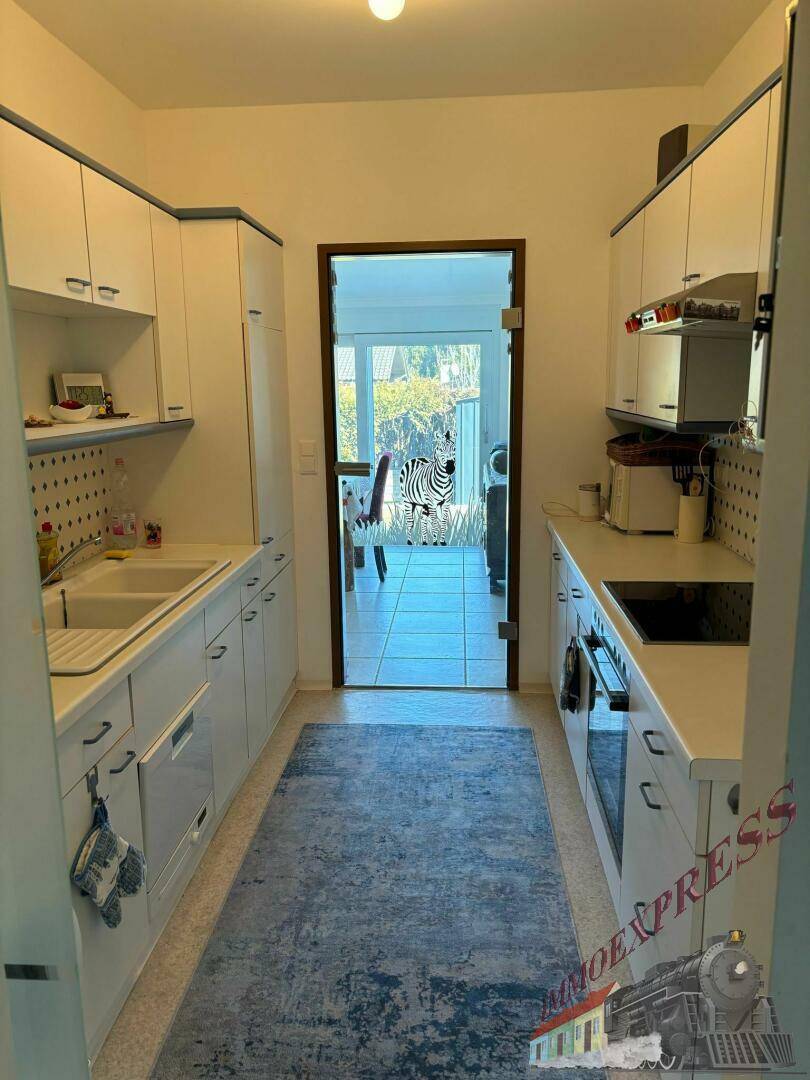 Schmale Küche mit weißen Schränken, Doppelspüle und Blick durch eine Glastür zum Essbereich.