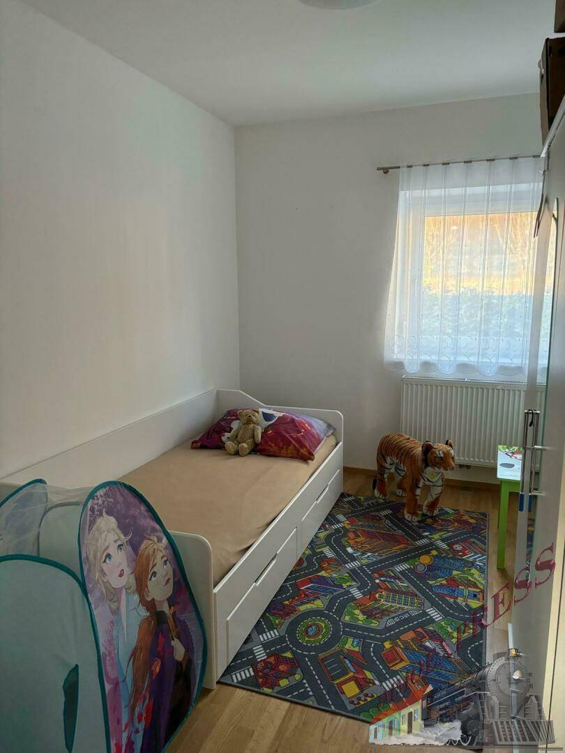 Kinderzimmer mit Einzelbett, farbenfrohem Teppich und einem Fenster für natürliches Licht.