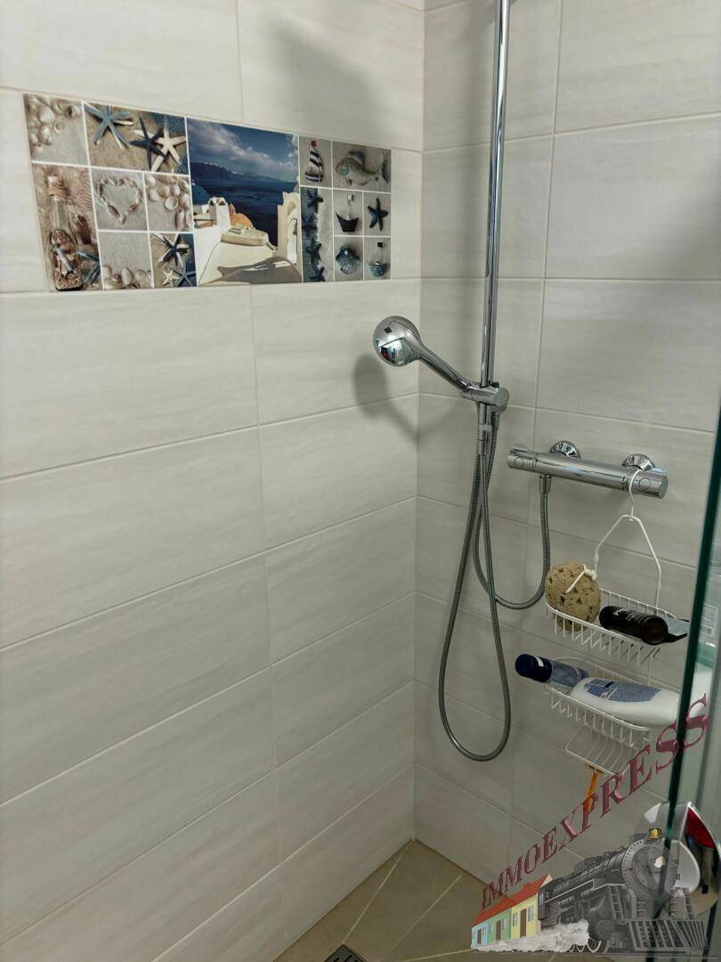 Duschbereich mit hellgrauen Fliesen und dekorativem Mosaik an der Wand.