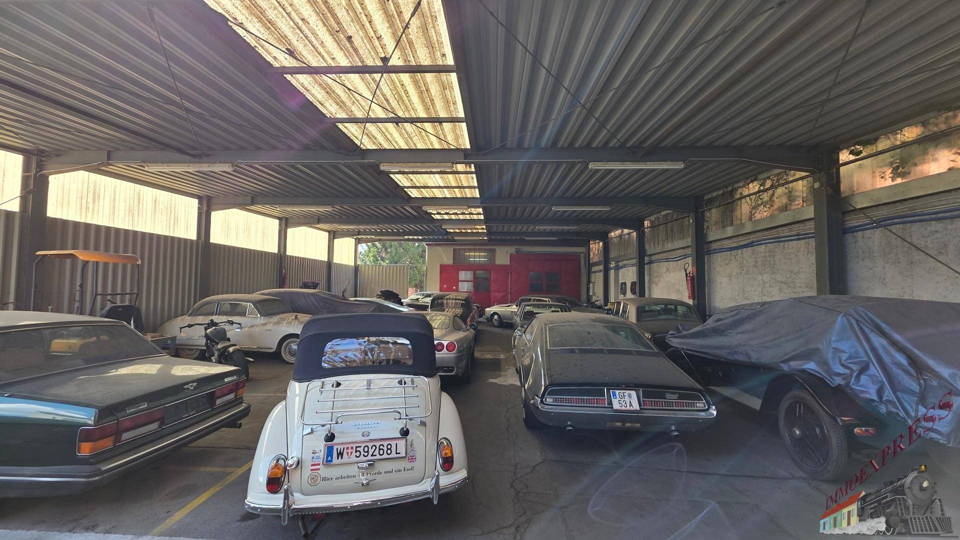 Große Halle mit Wellblechdach und vielen Oldtimern, einige davon abgedeckt.