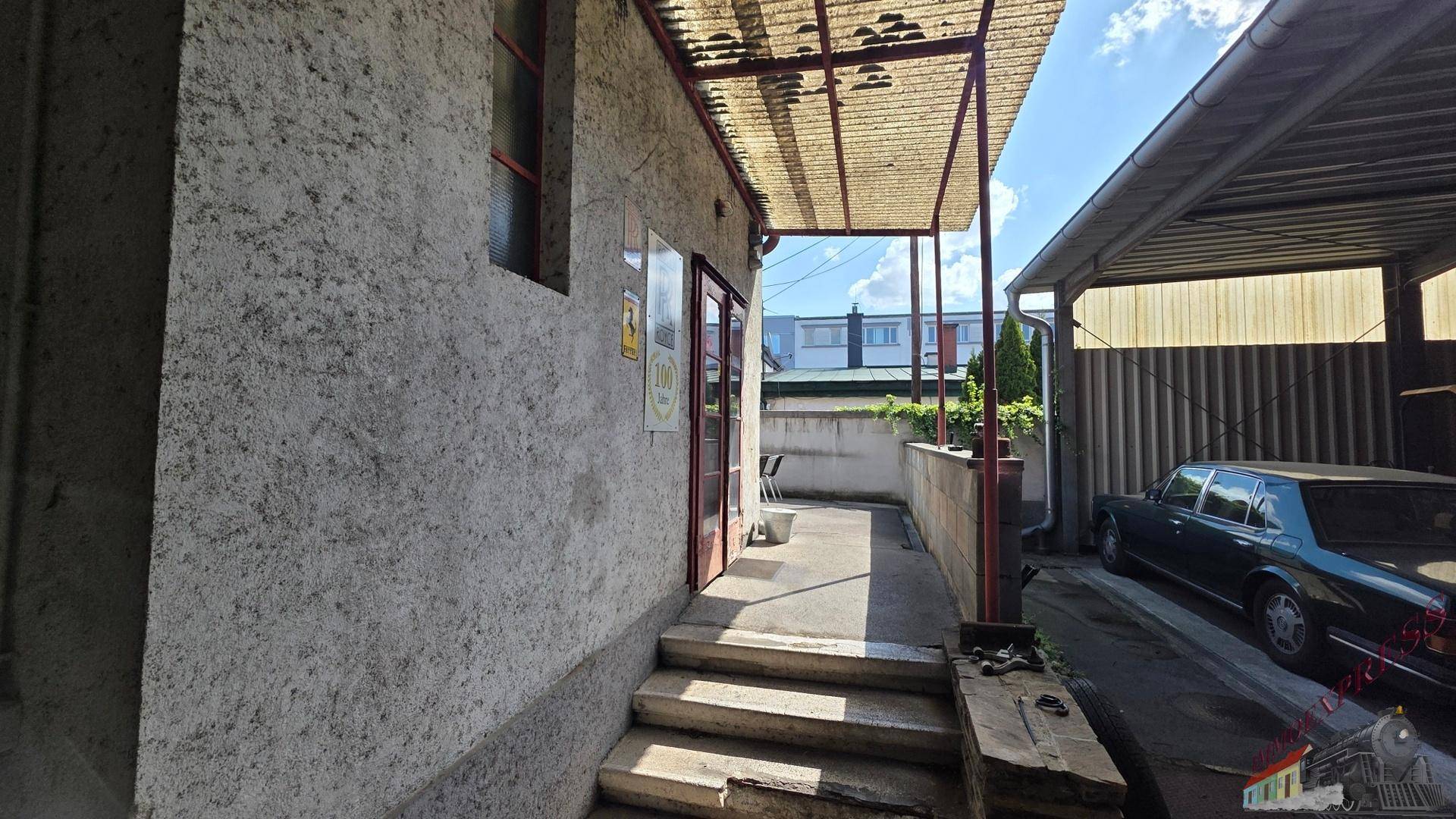 Eingangsbereich eines Gebäudes mit Betontreppe und Überdachung, daneben ein Carport.