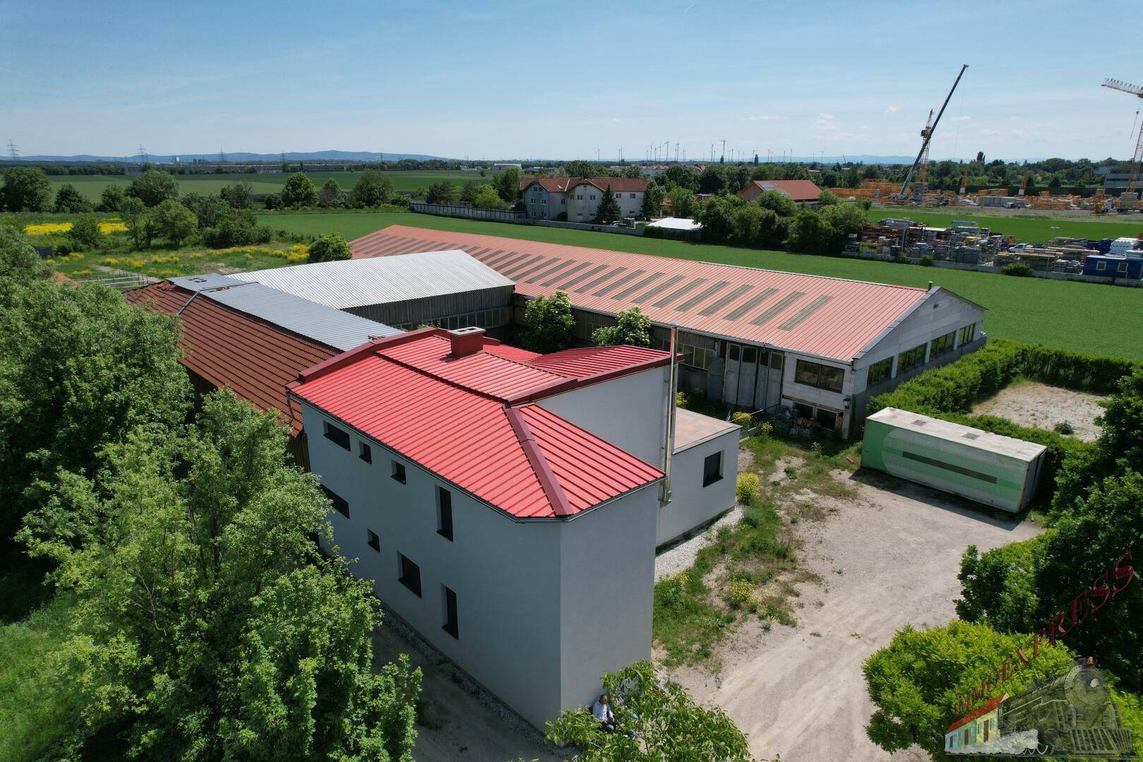 Luftaufnahme eines Gebäudekomplexes mit einem modernen weißen Haus und einer großen Halle mit rotem Dach.