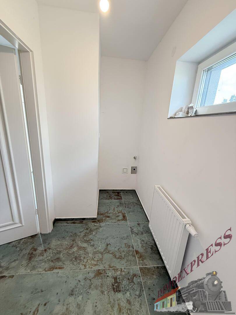 Heller Hauswirtschaftsraum mit Fenster, Heizkörper und Anschlüssen für Waschmaschine und Trockner.