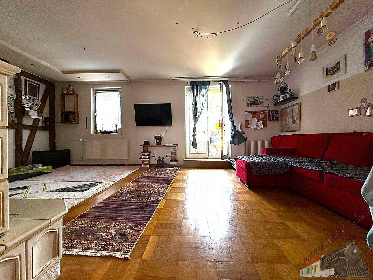 Helles Wohnzimmer mit Parkettboden, rotem Sofa und Zugang zu einem Außenbereich.