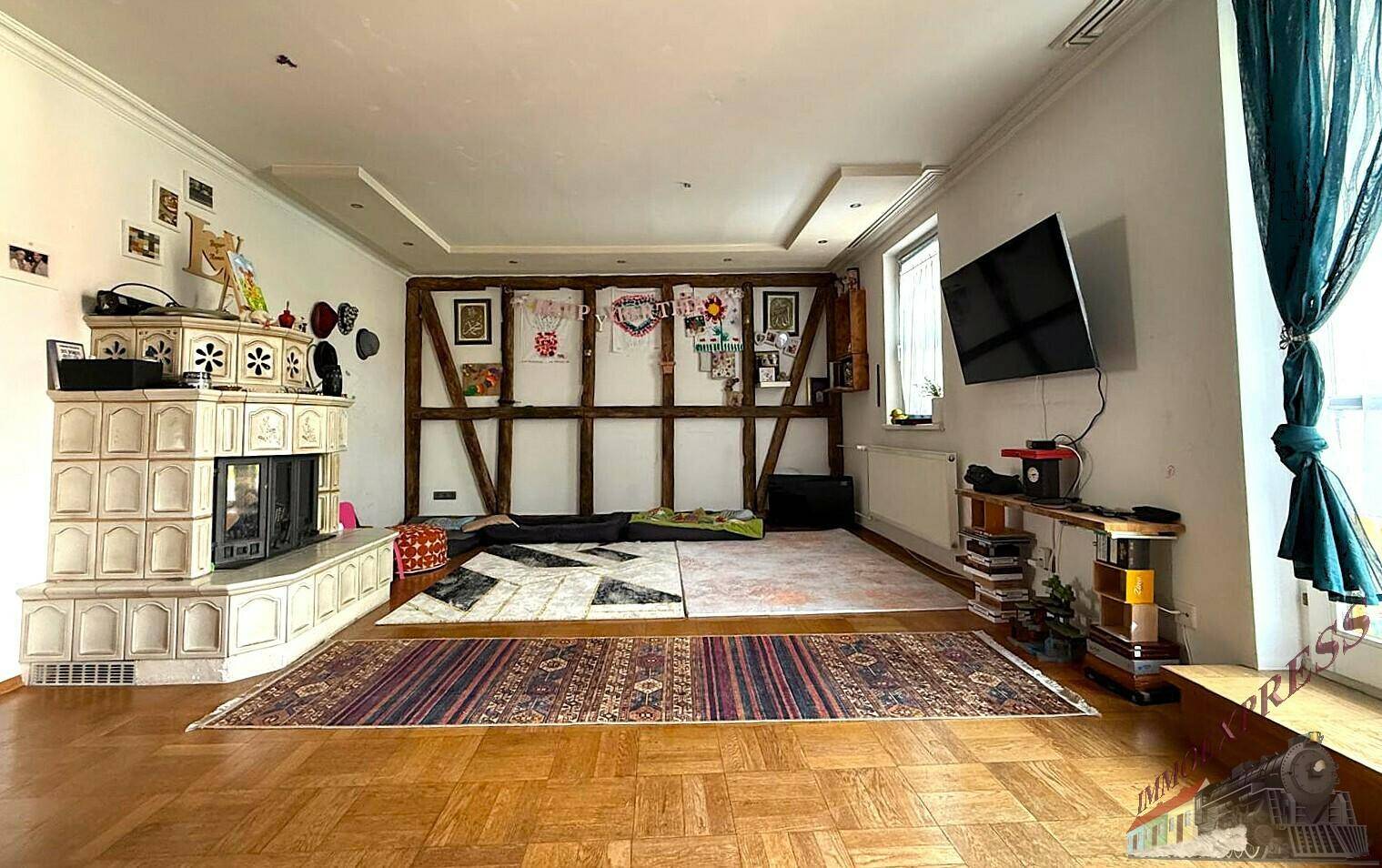 Geräumiges Wohnzimmer mit Parkettboden, Kachelofen und dekorativen Holzbalken an der Wand.