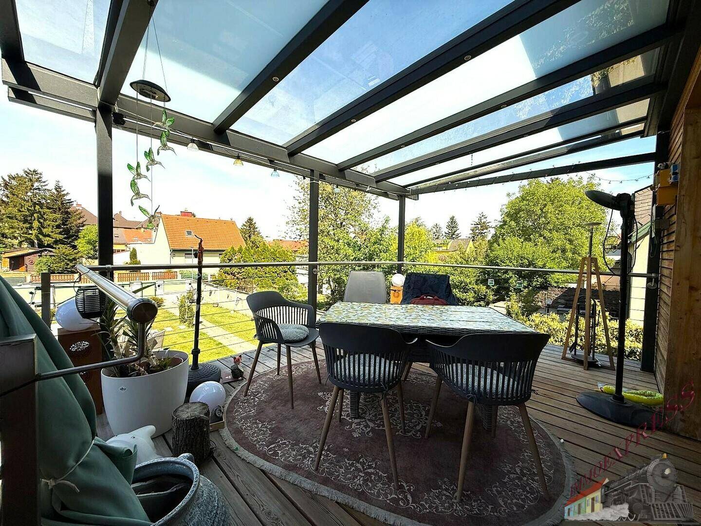 Überdachter Balkon mit Glasdach, Esstisch und Stühlen, bietet einen weiten Blick ins Grüne.