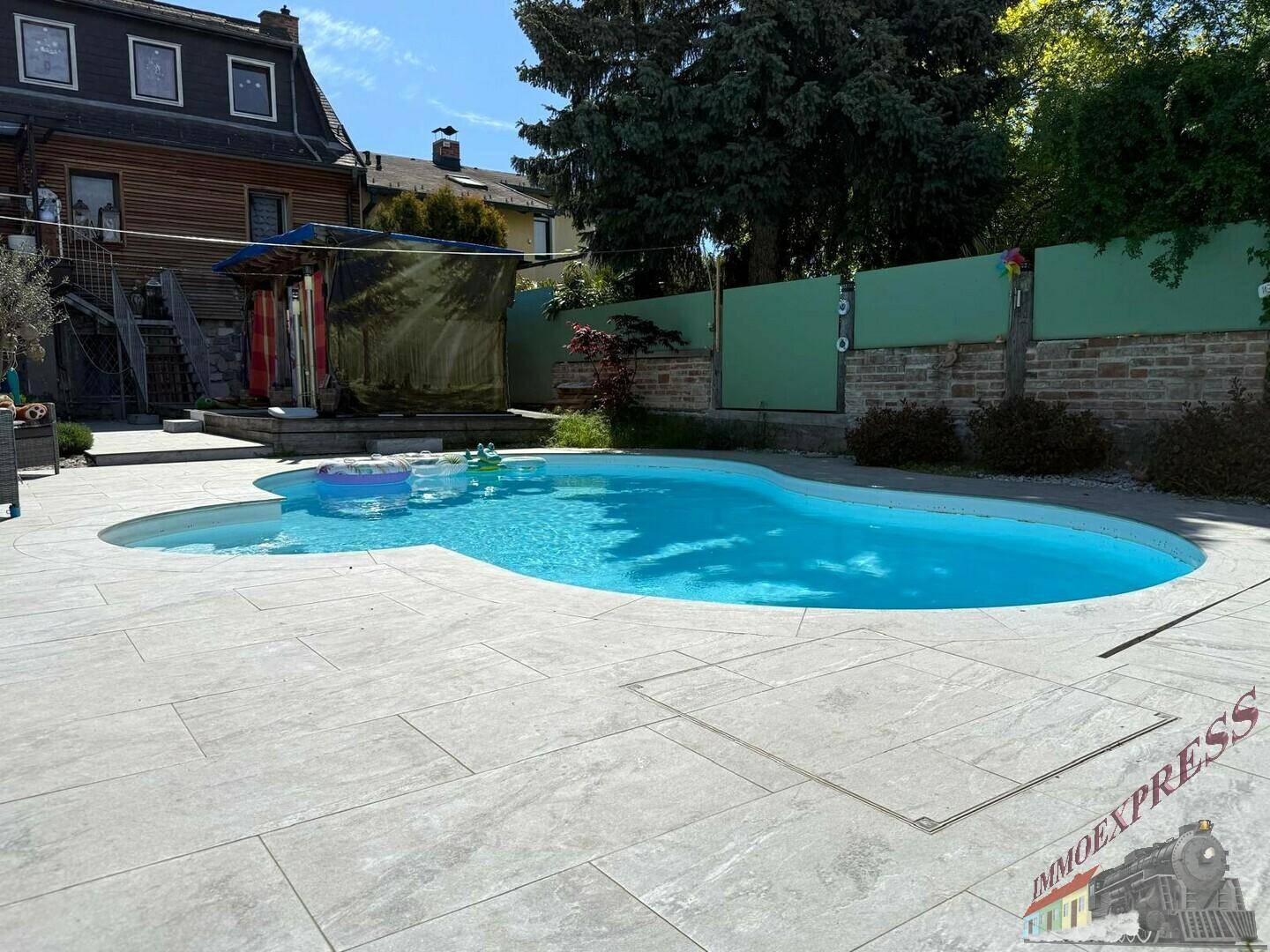 Großer, geschwungener Pool mit heller Steinumrandung und viel Platz zum Sonnenbaden.