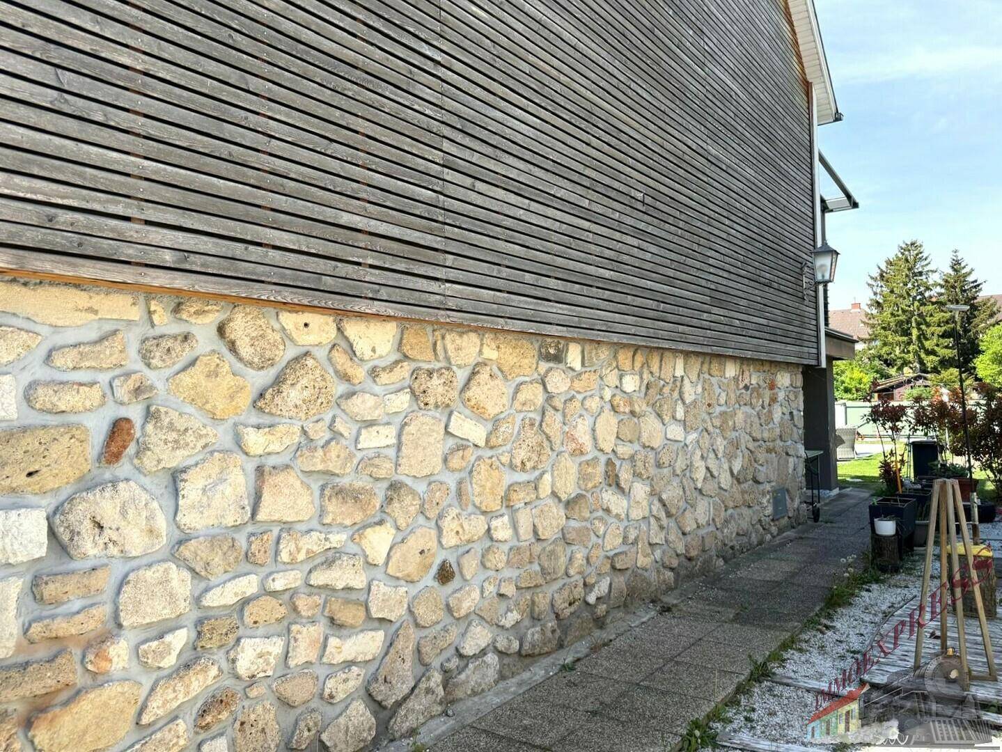 Seitenfassade des Hauses mit rustikaler Steinverkleidung im unteren Bereich und Holzverkleidung oben.