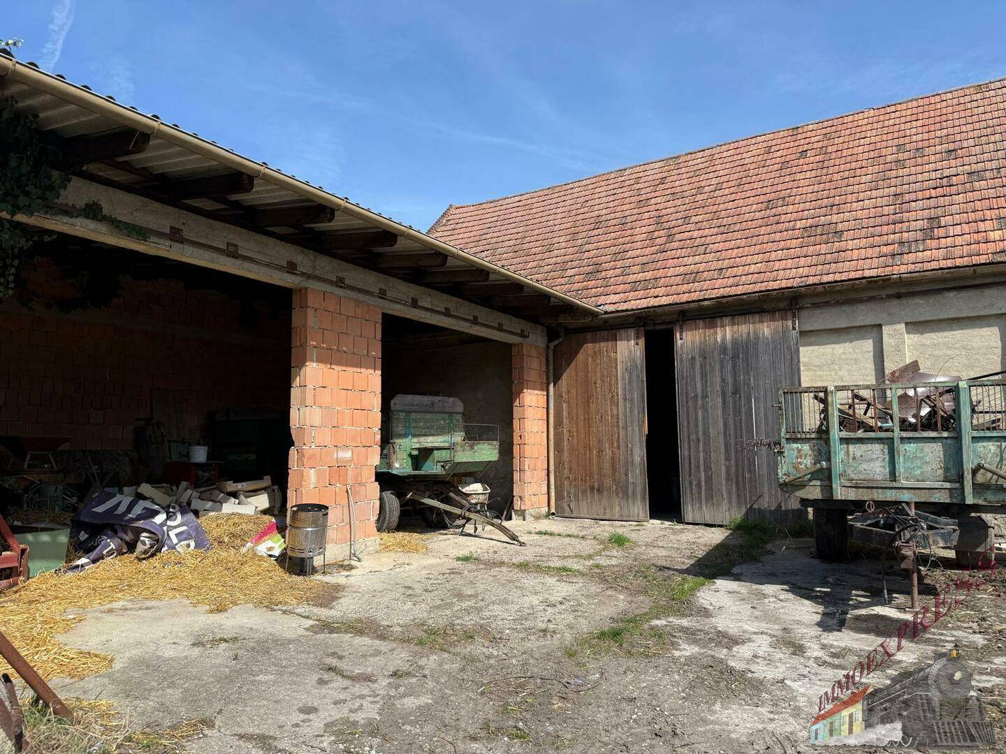 Scheunengebäude mit offenen Unterständen, Ziegelpfeilern und Holztoren auf einem ländlichen Hof.