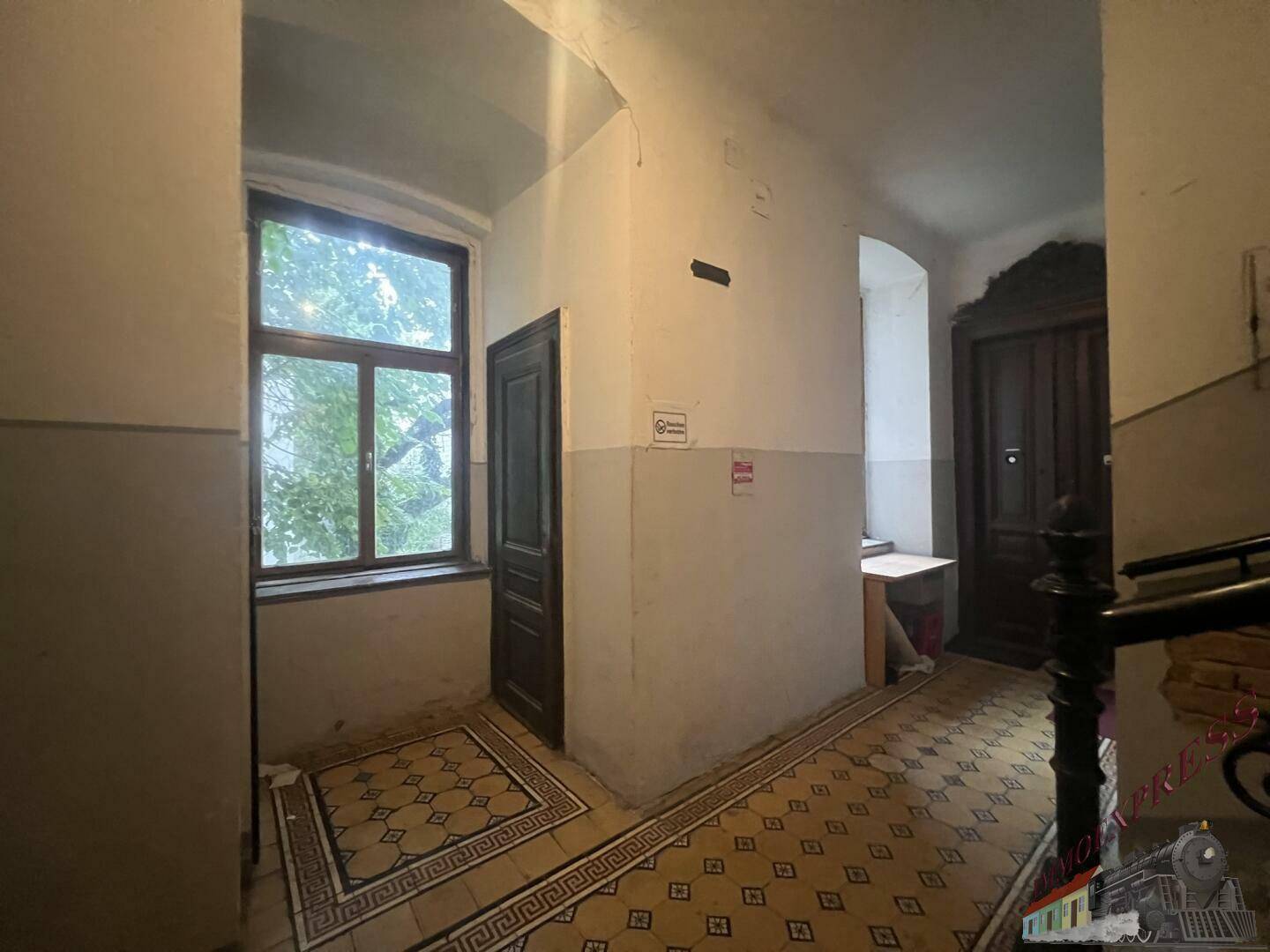 Heller Flur oder Treppenabsatz mit großem Fenster, Holztüren und gemusterten Fliesenboden.
