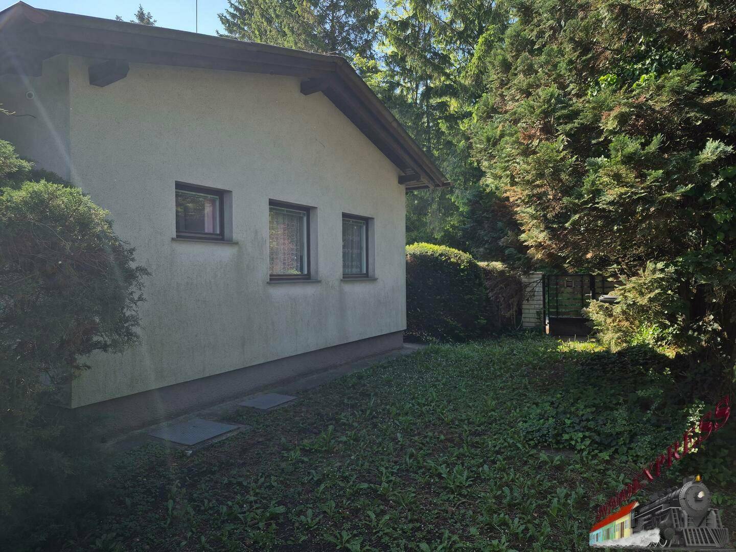 Seitenansicht des Hauses mit Garten und hohen Bäumen.