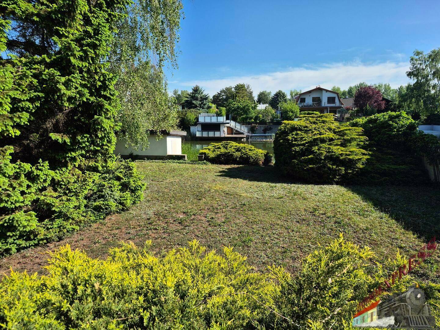 Großer Garten mit Rasenfläche, Büschen und Blick auf den See.