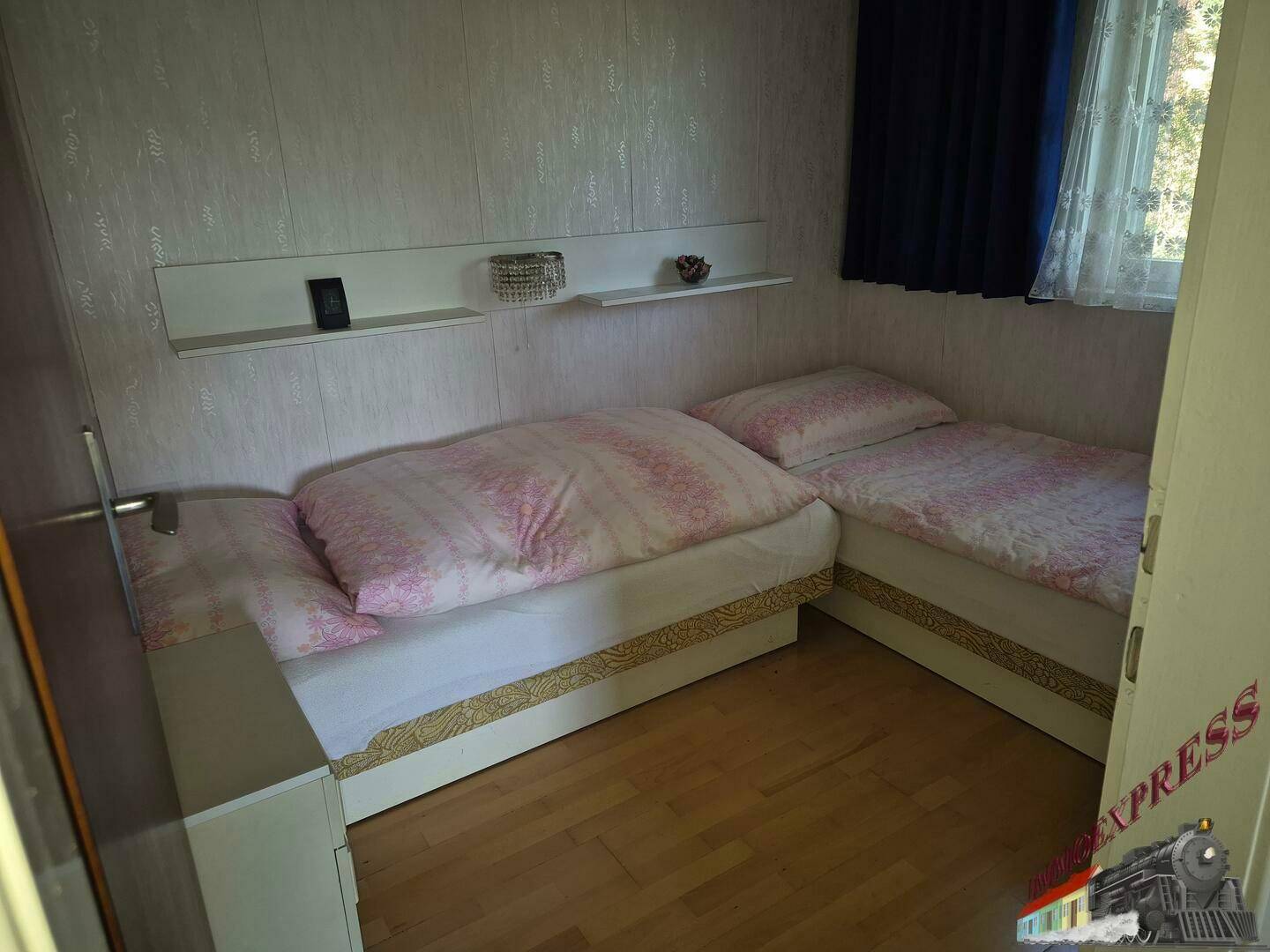 Helles Schlafzimmer mit zwei Betten, Holzfußboden und Blick ins Grüne.