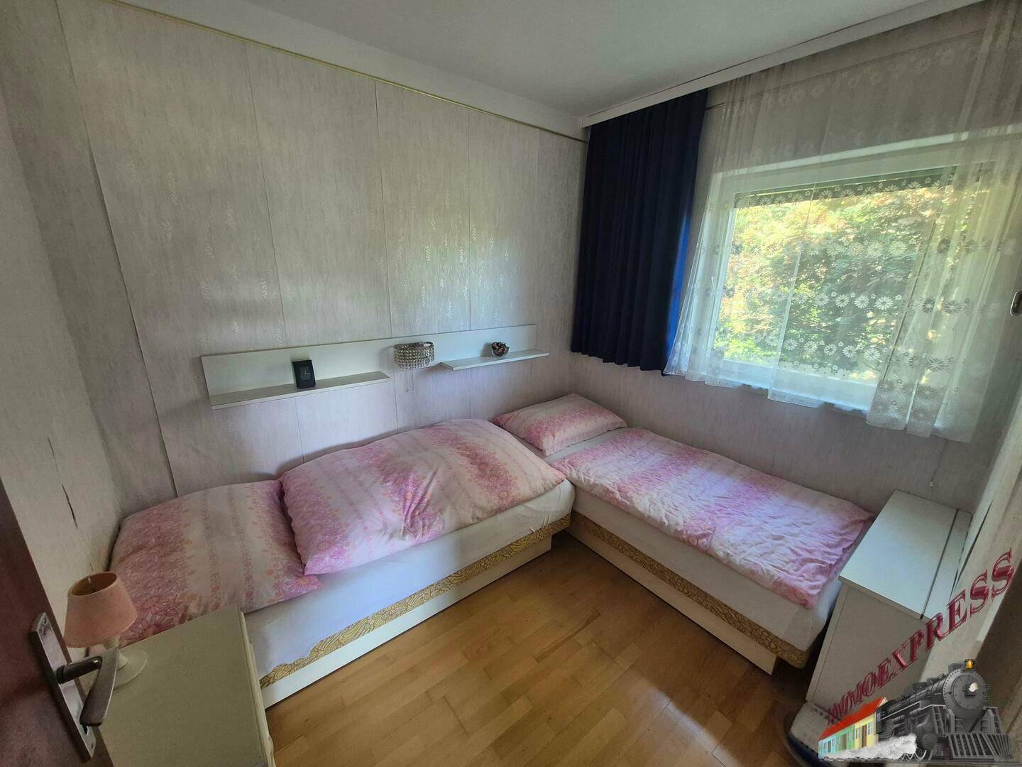 Schlafzimmer mit zwei Einzelbetten, Holzfußboden und Fenster.
