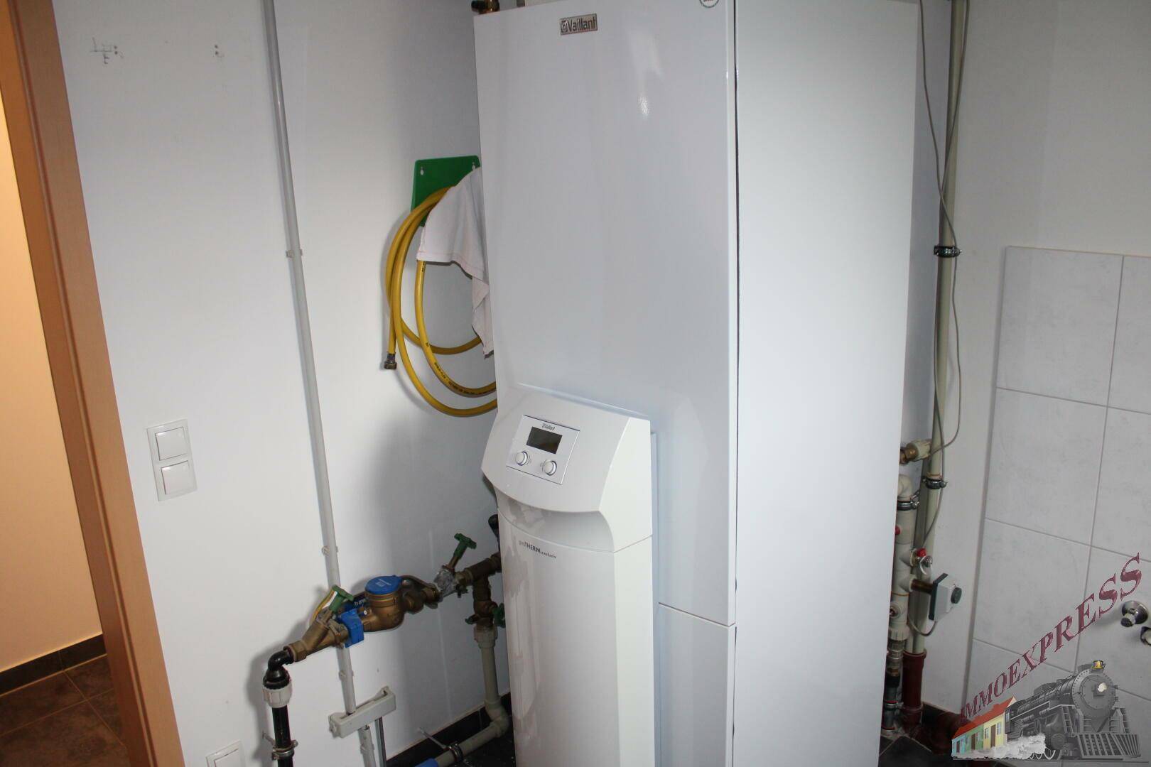 Große Heizungsanlage mit Warmwasserspeicher und Wasserleitungen in einem Hauswirtschaftsraum.