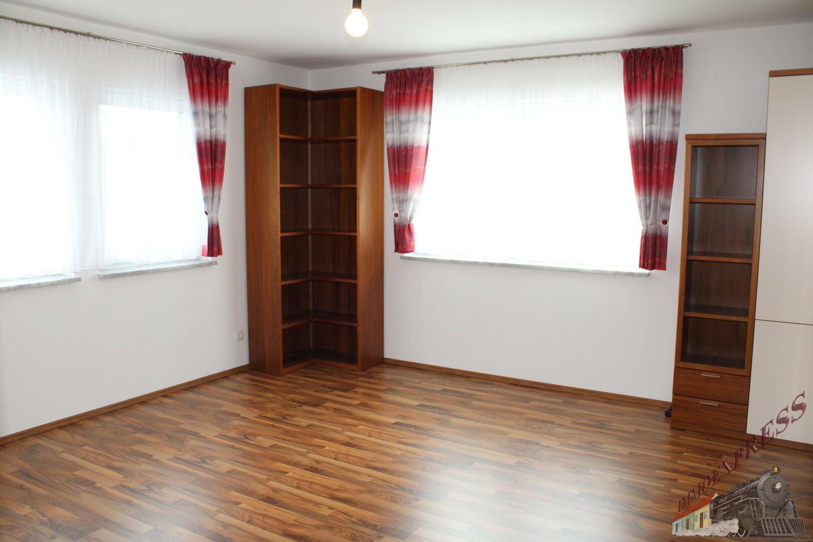 Schlafzimmer mit Laminatboden, zwei Fenstern und Holzregalen.