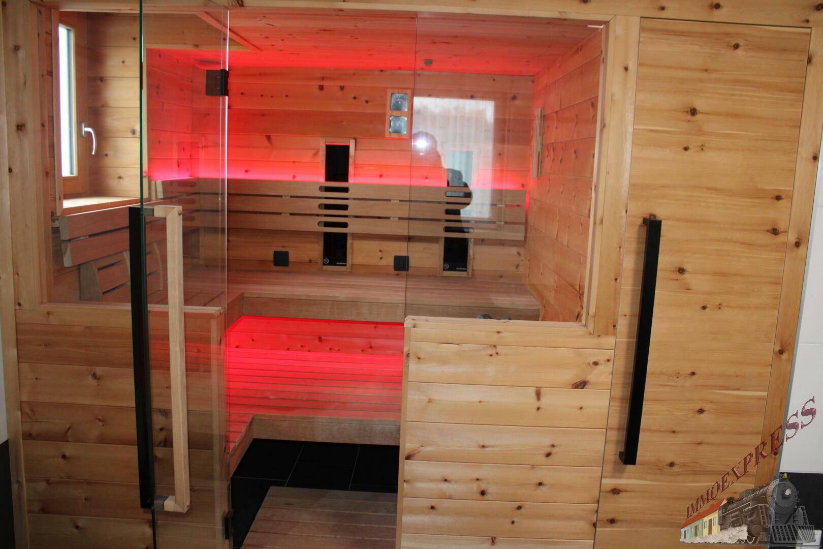 Innenansicht der Holzsauna mit roter Beleuchtung und Sitzbänken.