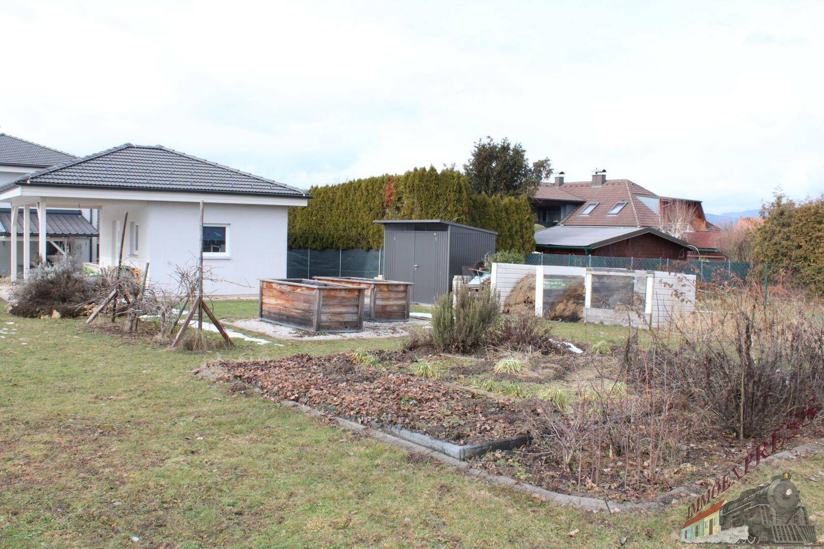 Gartenbereich mit Hochbeeten, Schuppen und Hecke im Hintergrund.