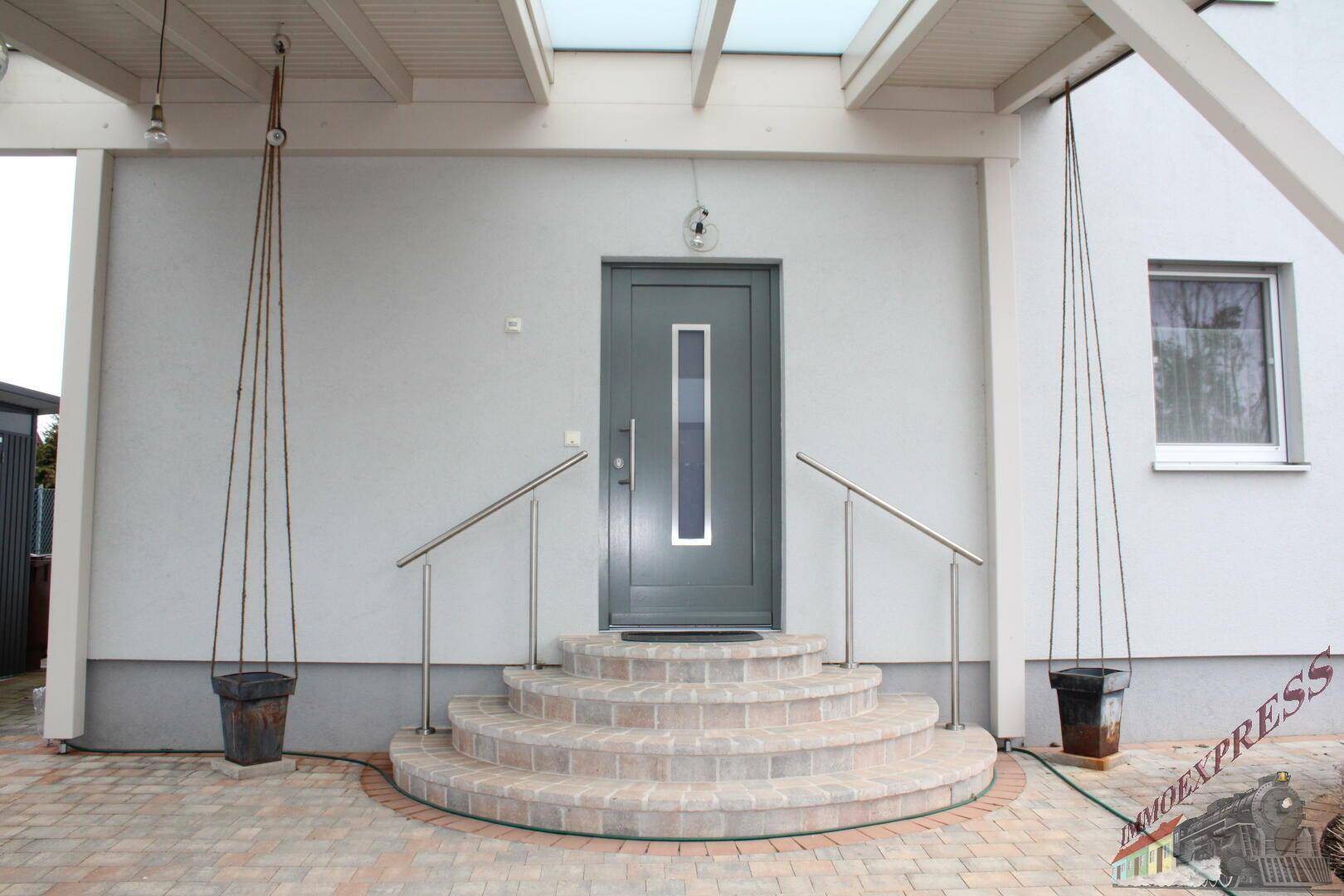 Eingangstür des Hauses mit Stufen, Edelstahlgeländer und Überdachung.