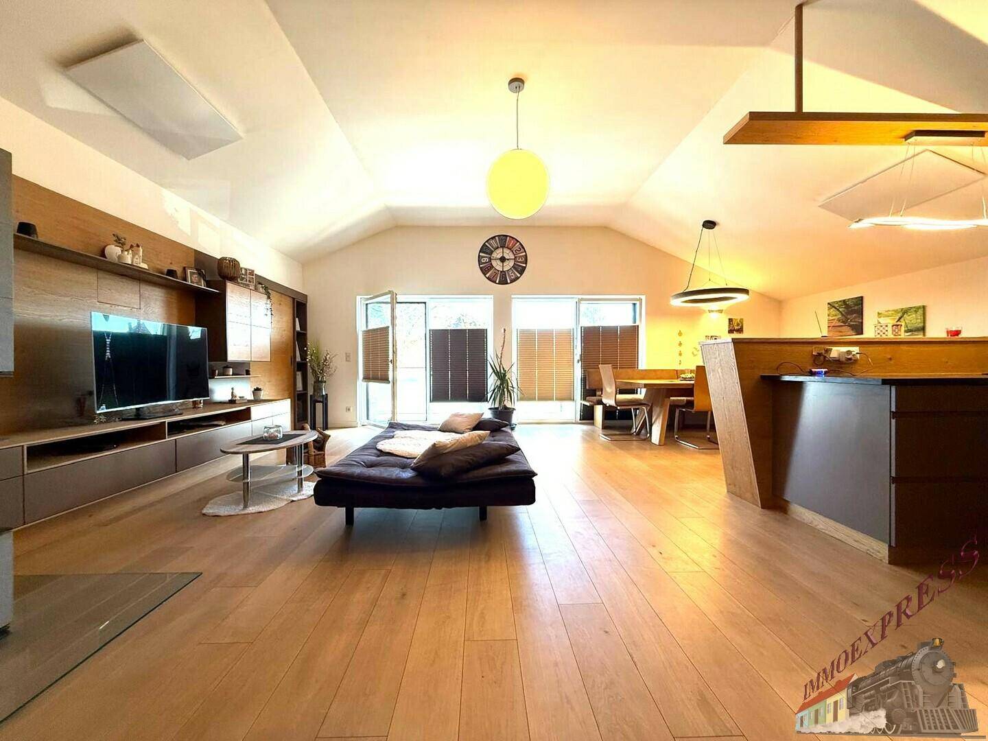 Offener Wohn- und Essbereich mit Holzboden, gemütlichem Sofa und viel Tageslicht.