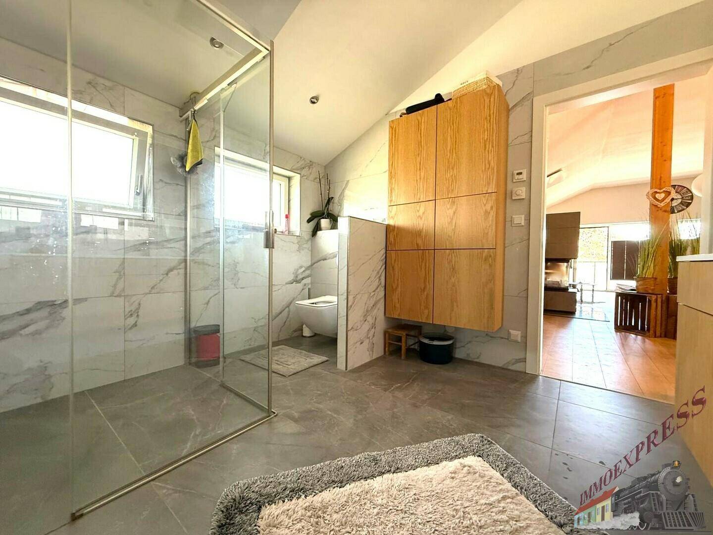 Modernes Badezimmer mit großformatigen Marmorfliesen, begehbarer Dusche und Holzschränken.
