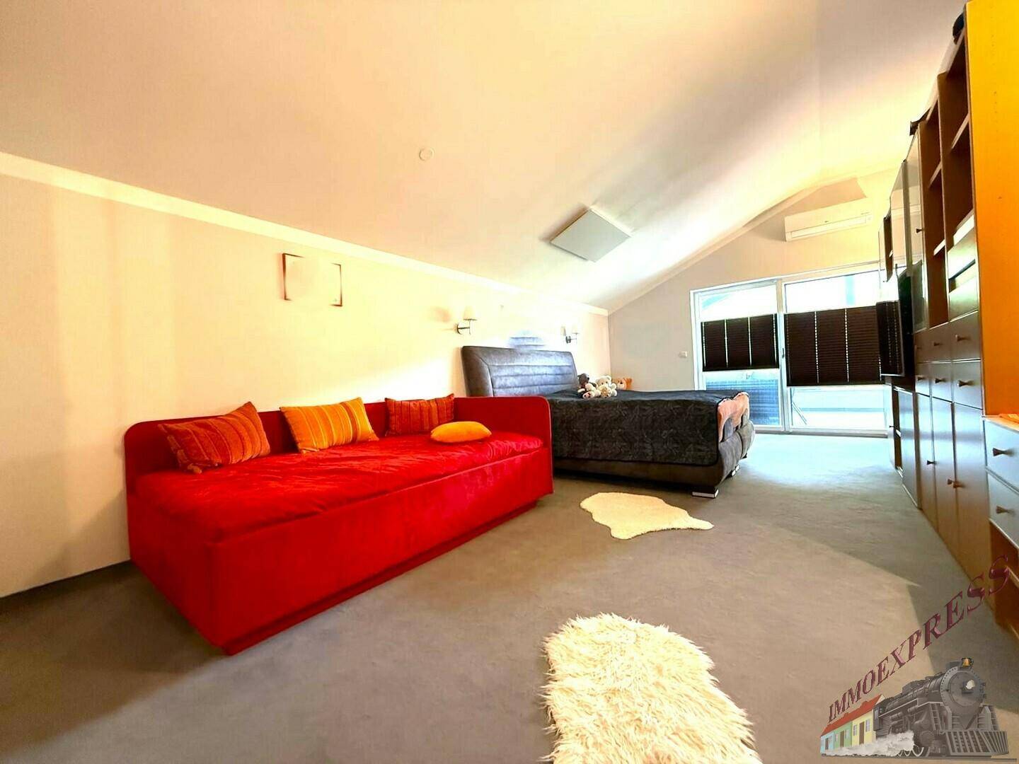 Geräumiges Schlafzimmer mit rotem Sofa, großem Bett und Dachschrägen, die Gemütlichkeit verleihen.