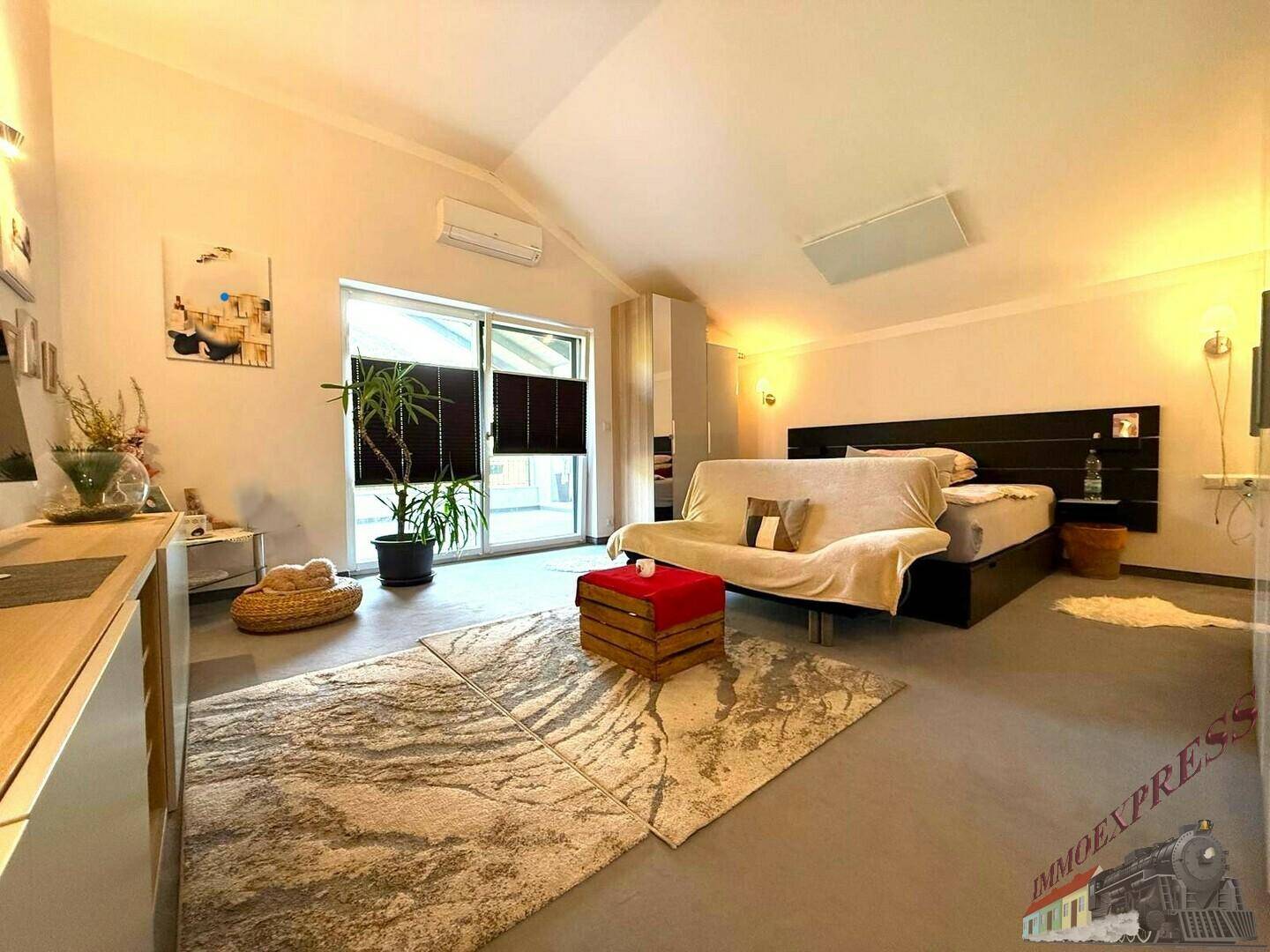 Helles Schlafzimmer mit Doppelbett, Sofa, Teppichboden und Zugang zu einem Balkon.
