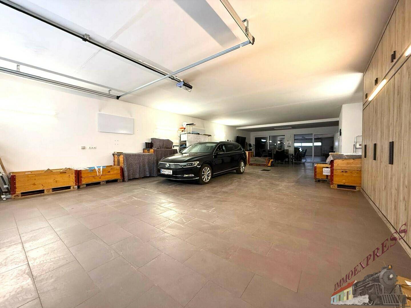 Große Garage mit Fliesenboden, einem geparkten Auto und Holzregalen für Lagerzwecke.