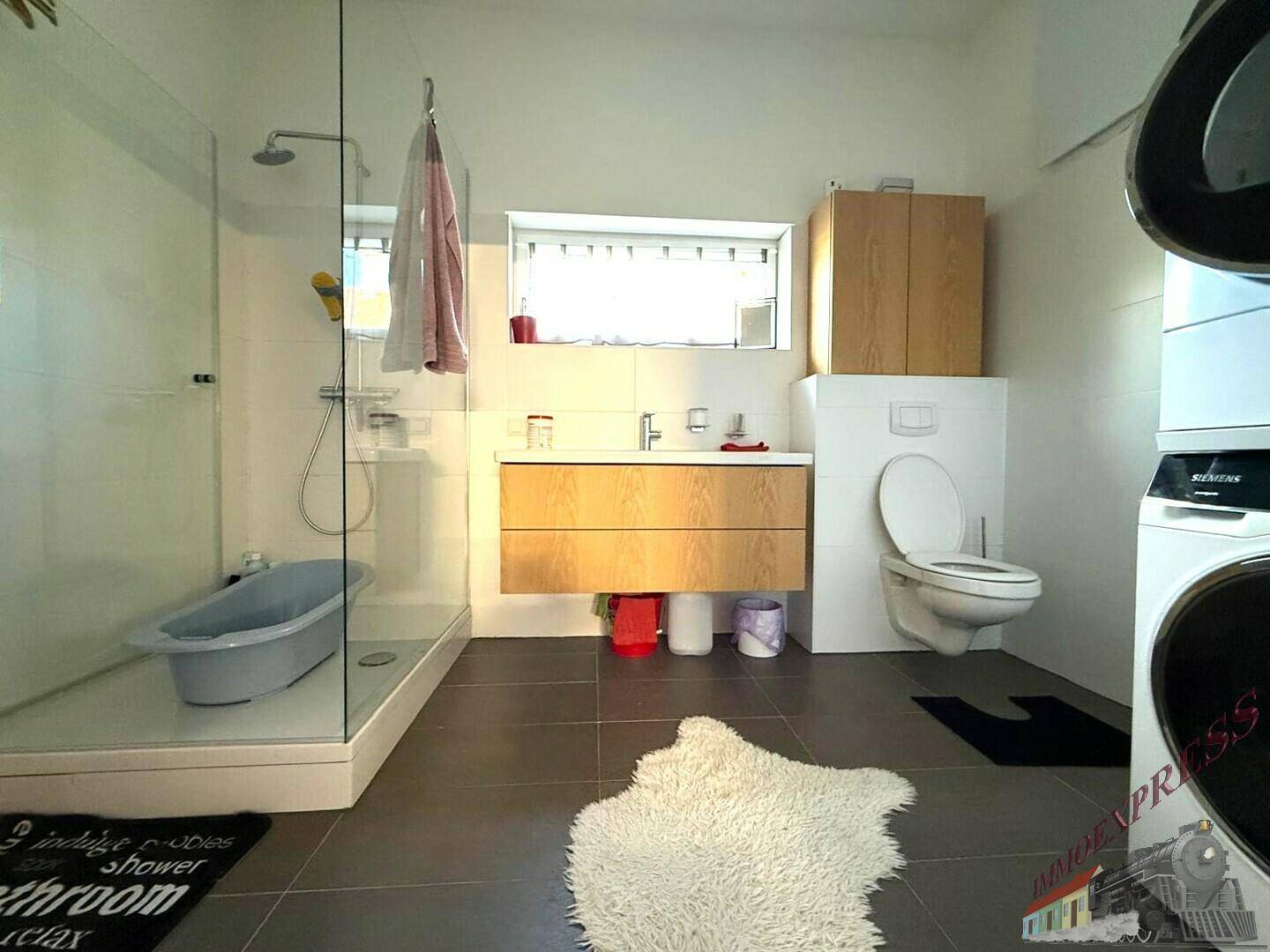 Funktionales Badezimmer mit ebenerdiger Dusche, Toilette und integrierten Waschmaschinen.