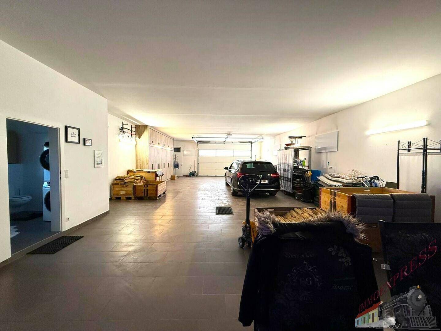 Geräumige Garage mit viel Stauraum, einem geparkten Auto und Zugang zu einem Nebenraum.